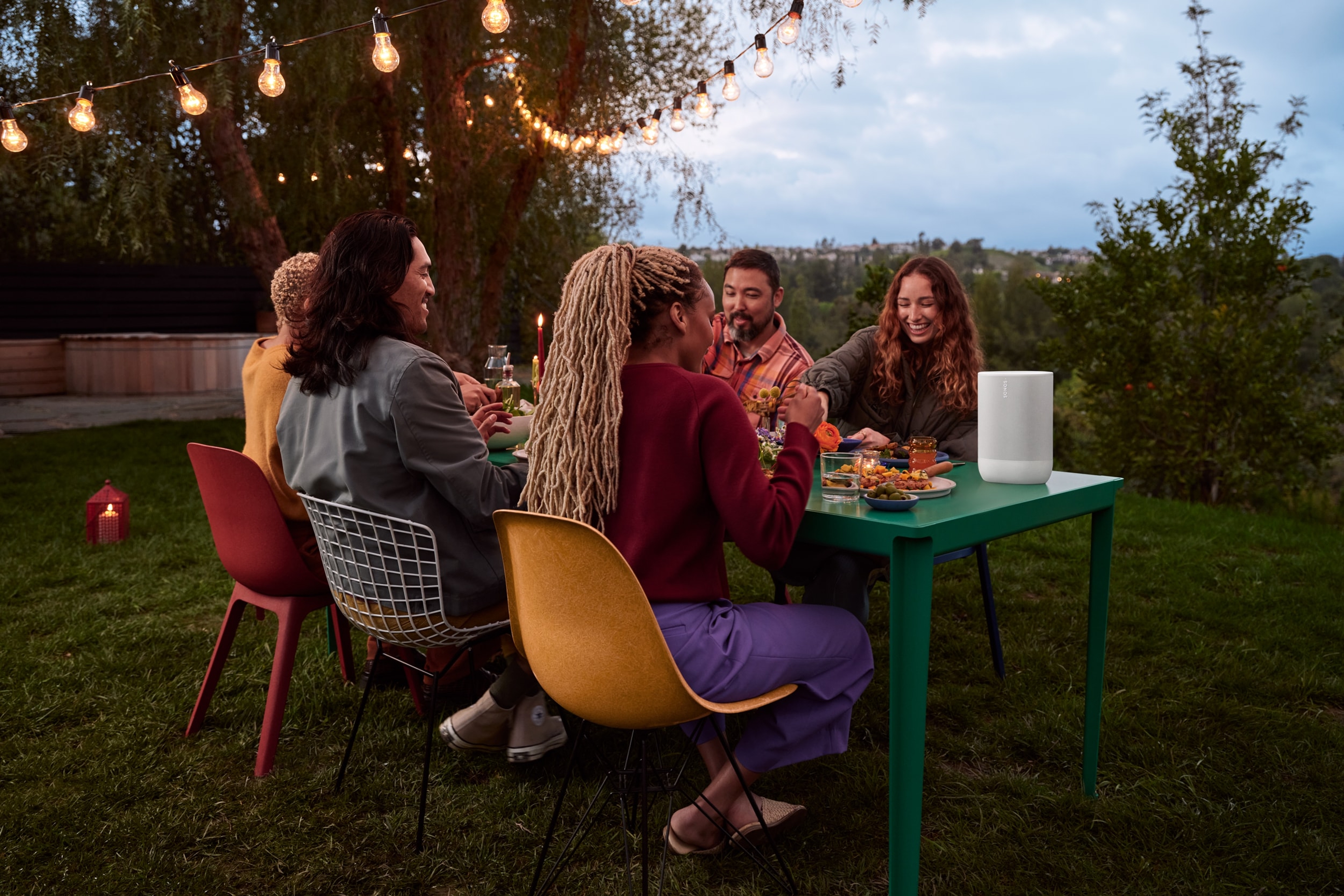 Image of a group of friends at a backyard dinner party with a white Sonos Move 2 on the table