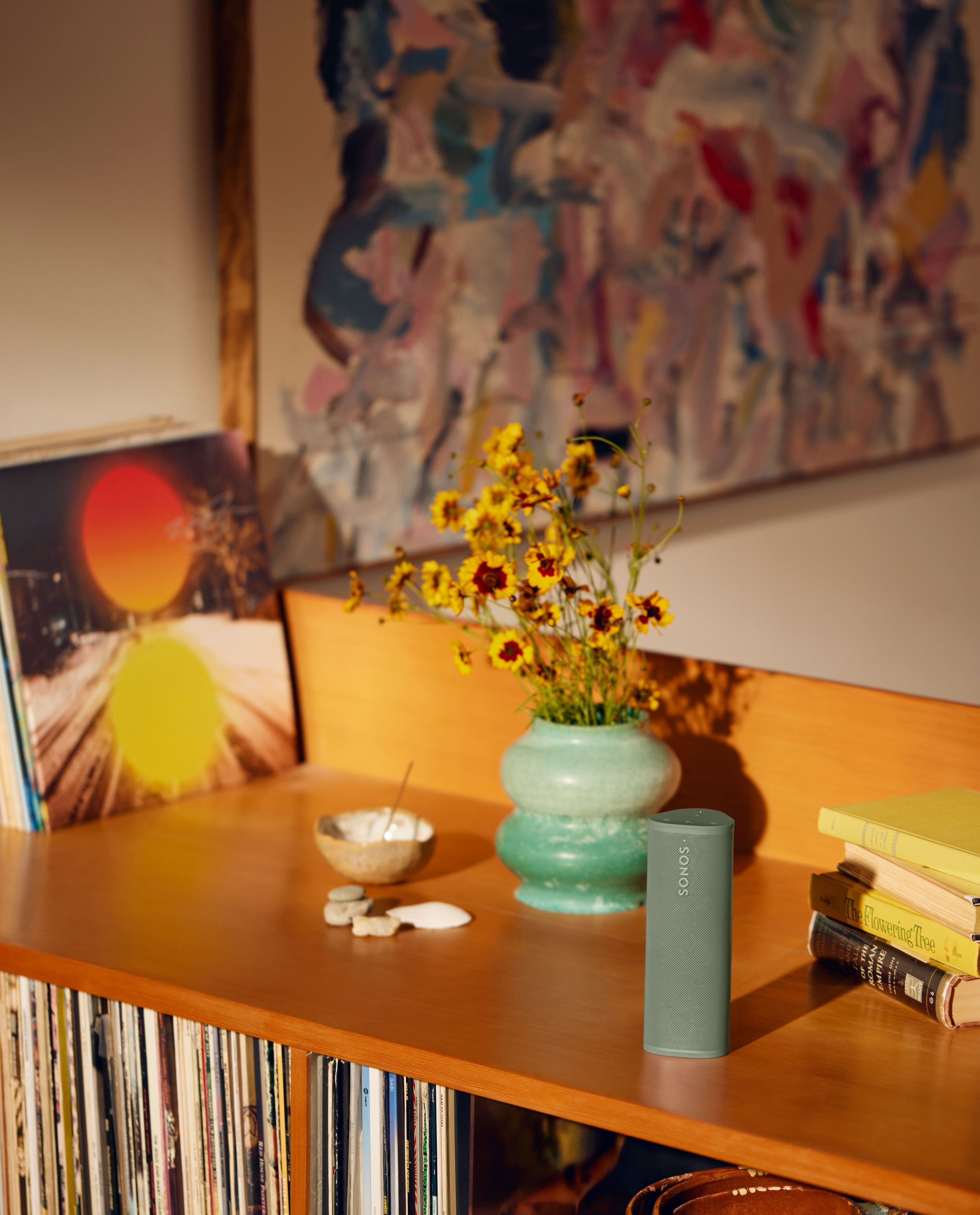 Grøn Sonos Roam 2 på et møbel ved siden af en vase med blomster og bøger