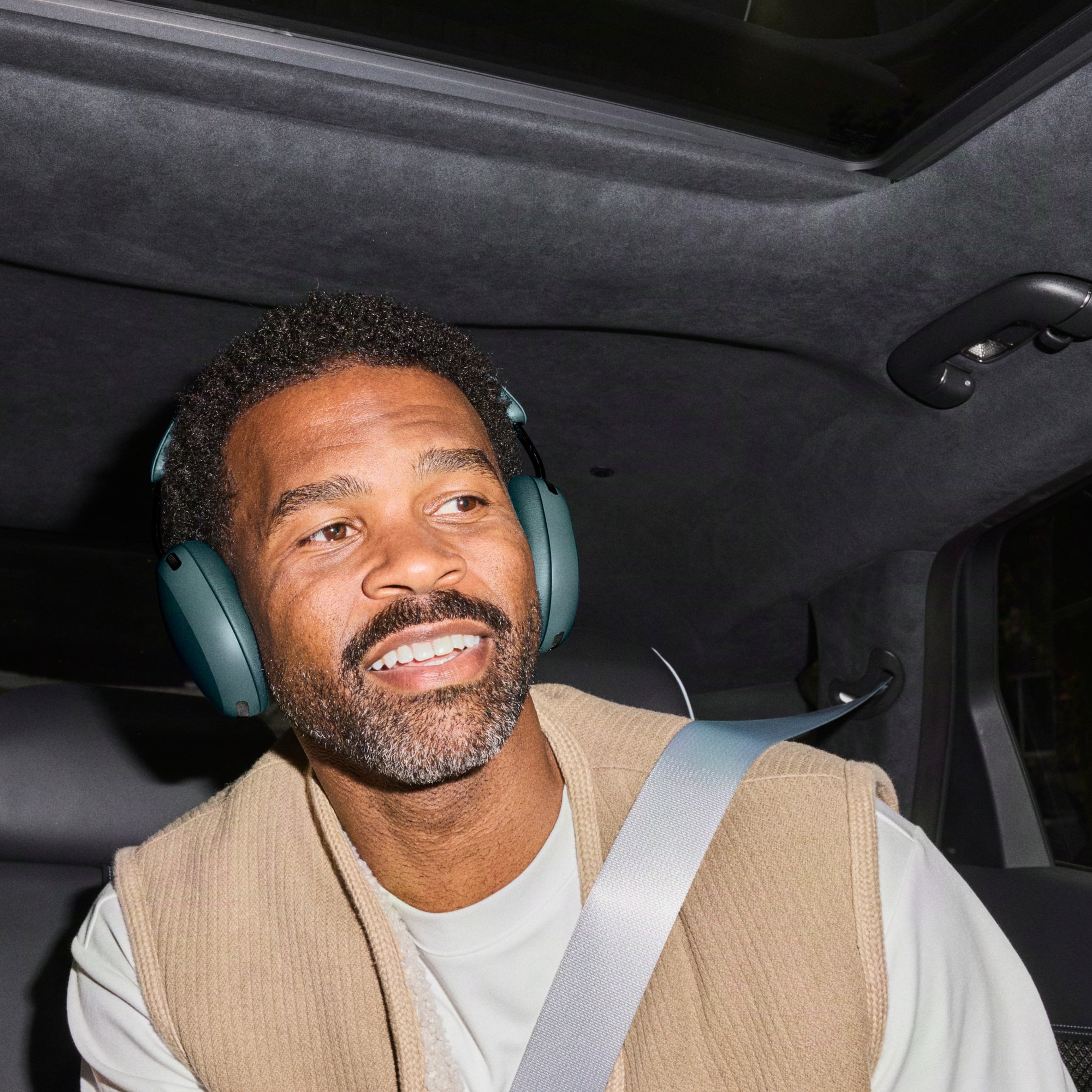 Person riding in the back seat of a car wearing Sonos Ace Ultra headphones in Agave