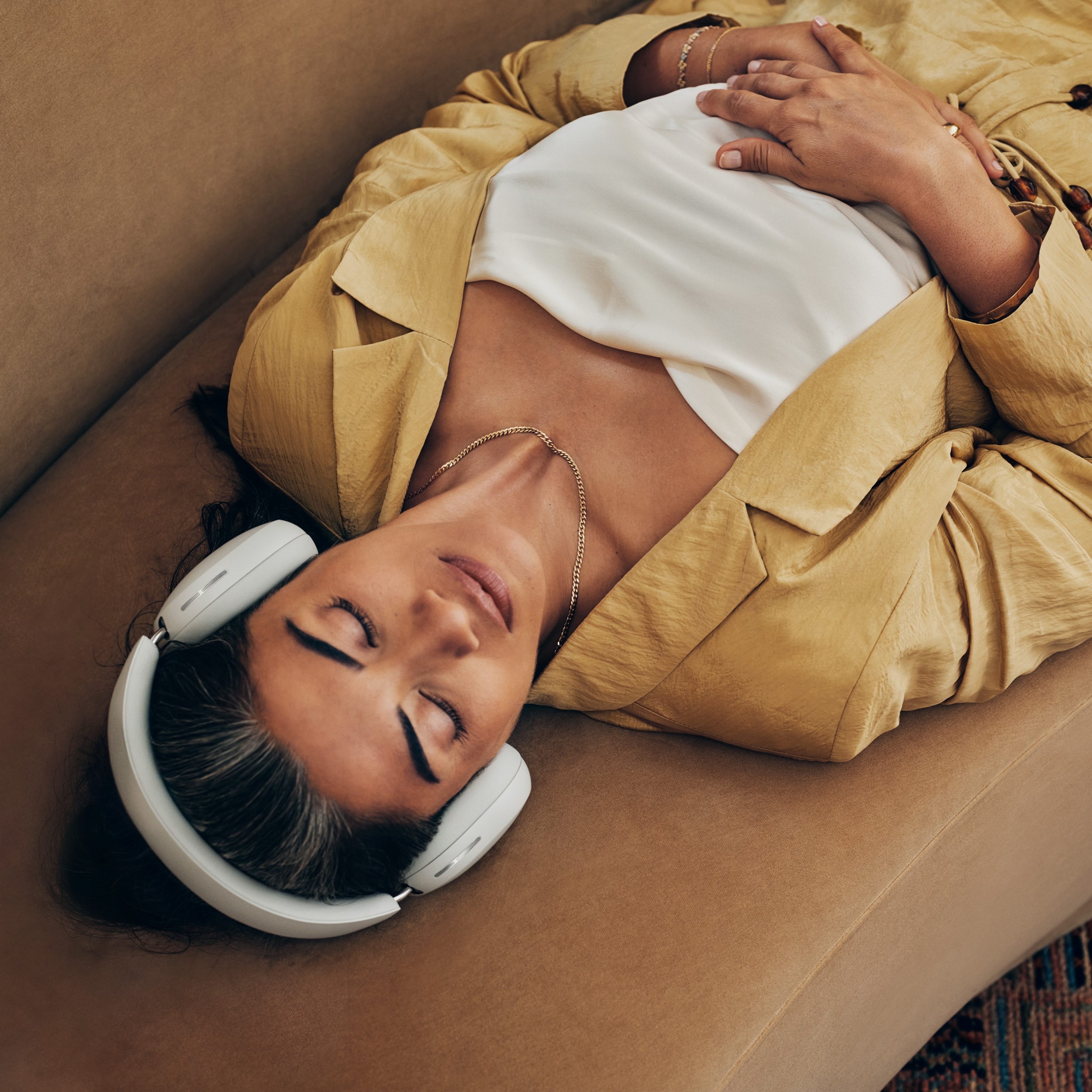 Une femme allongée sur un canapé porte un casque audio Sonos Ace couleur Soft White