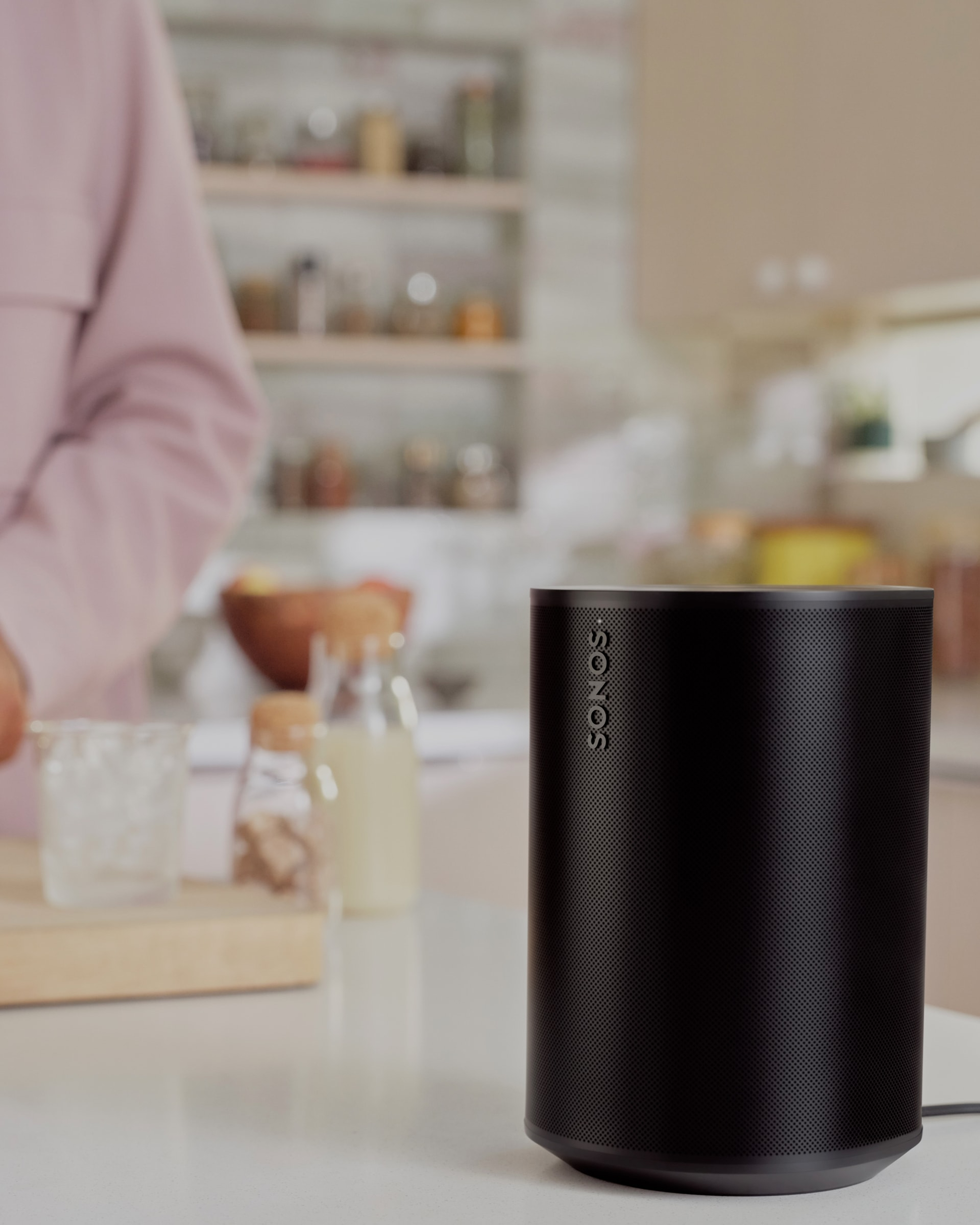 Closeup of a black Era 100 speaker on a kitchen counter while someone makes coffee in the background