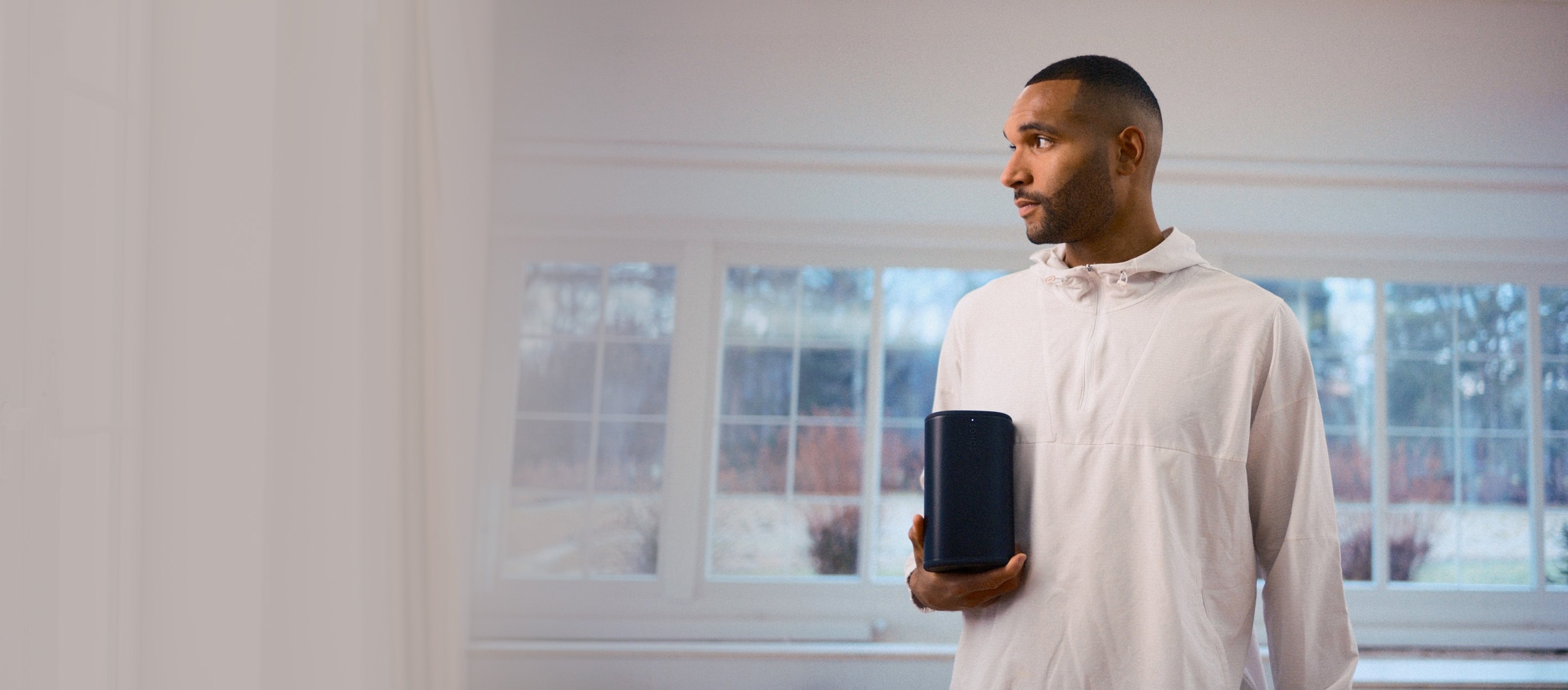 German footballer Jonathan Tah holding a black Sonos Play speaker in his home