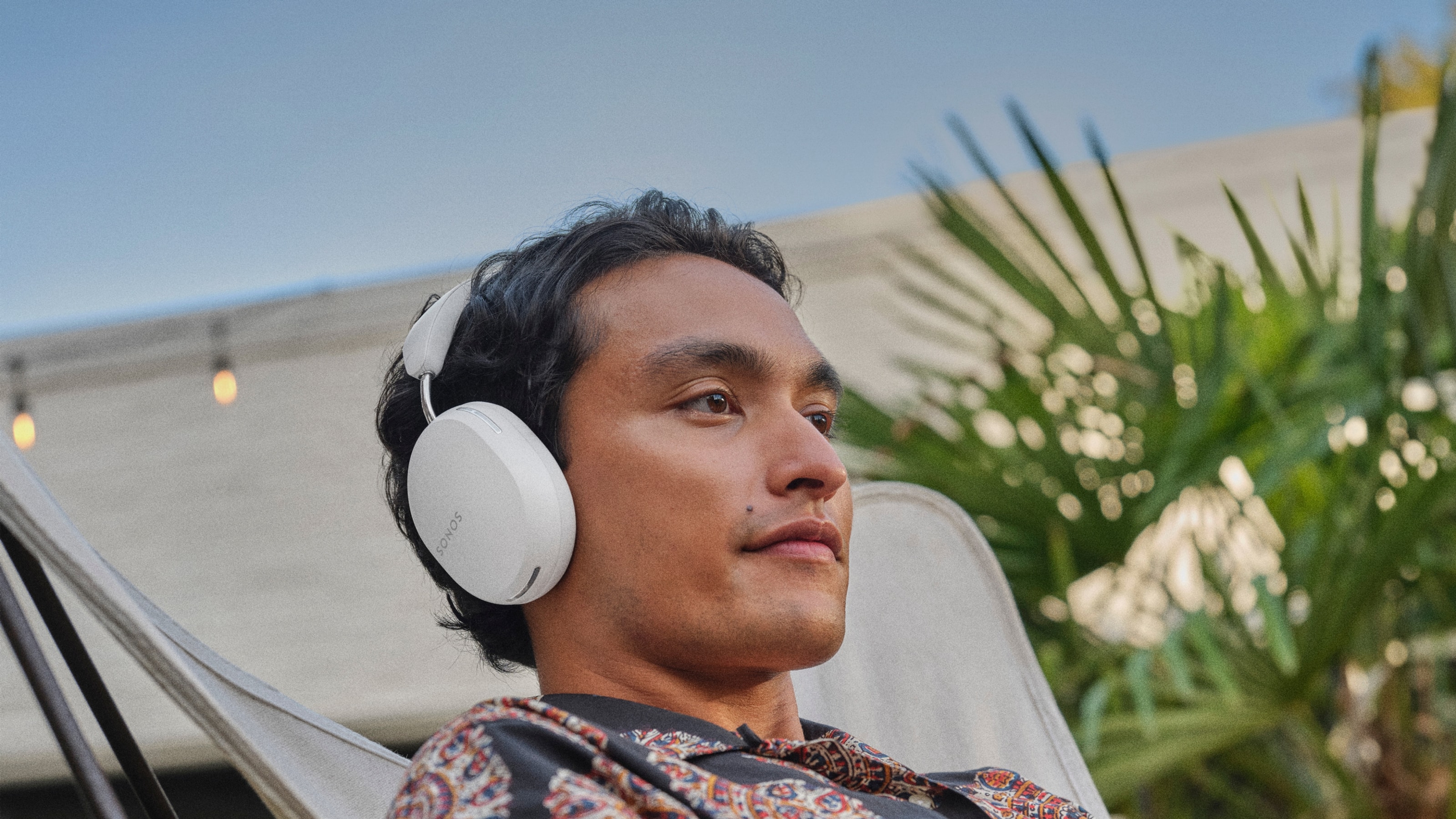 Person listening to music on a white Sonos Ace headphones outdoors