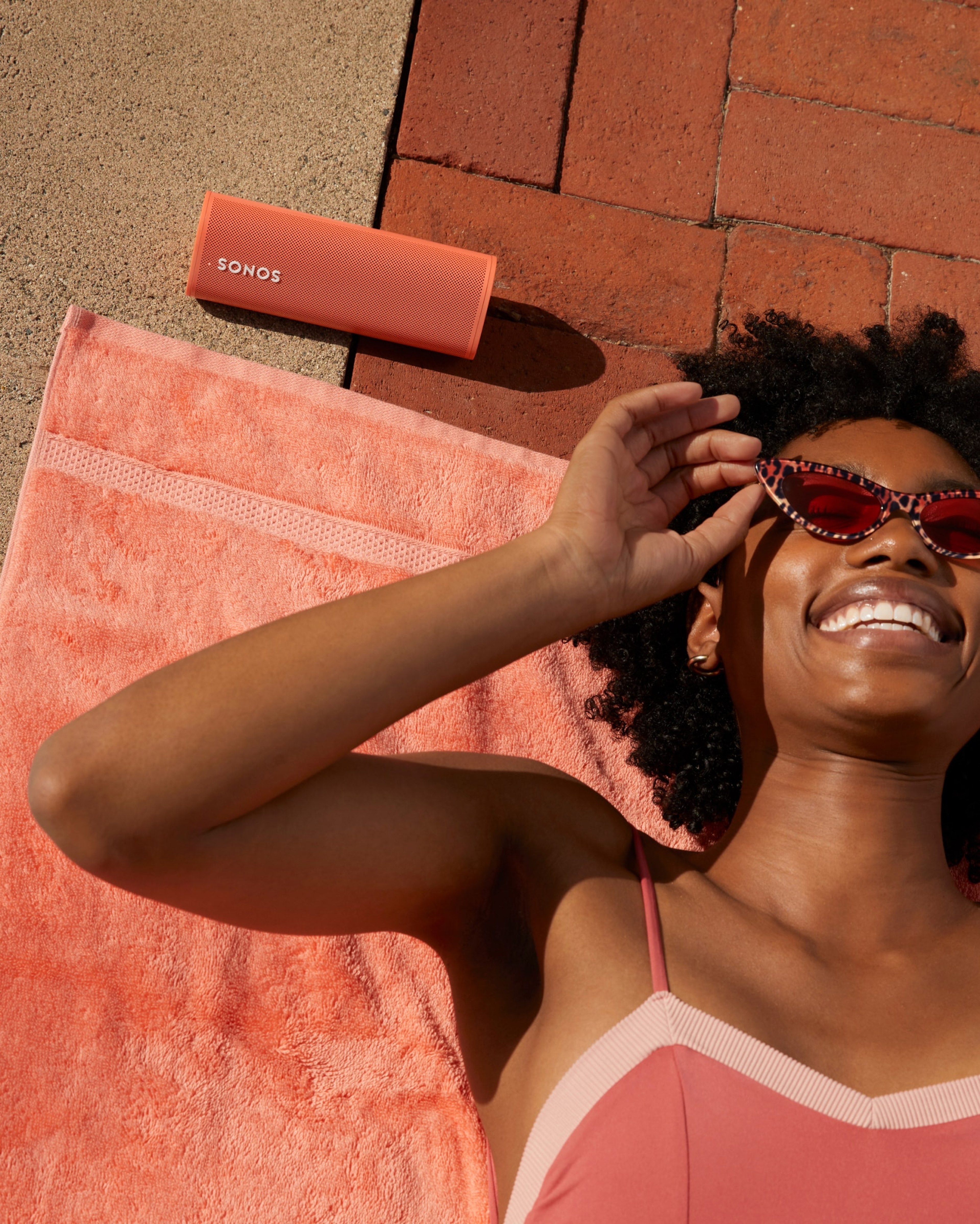 Femme allongée au bord d'une piscine écoutant de la musique avec le Sonos Roam Sunset