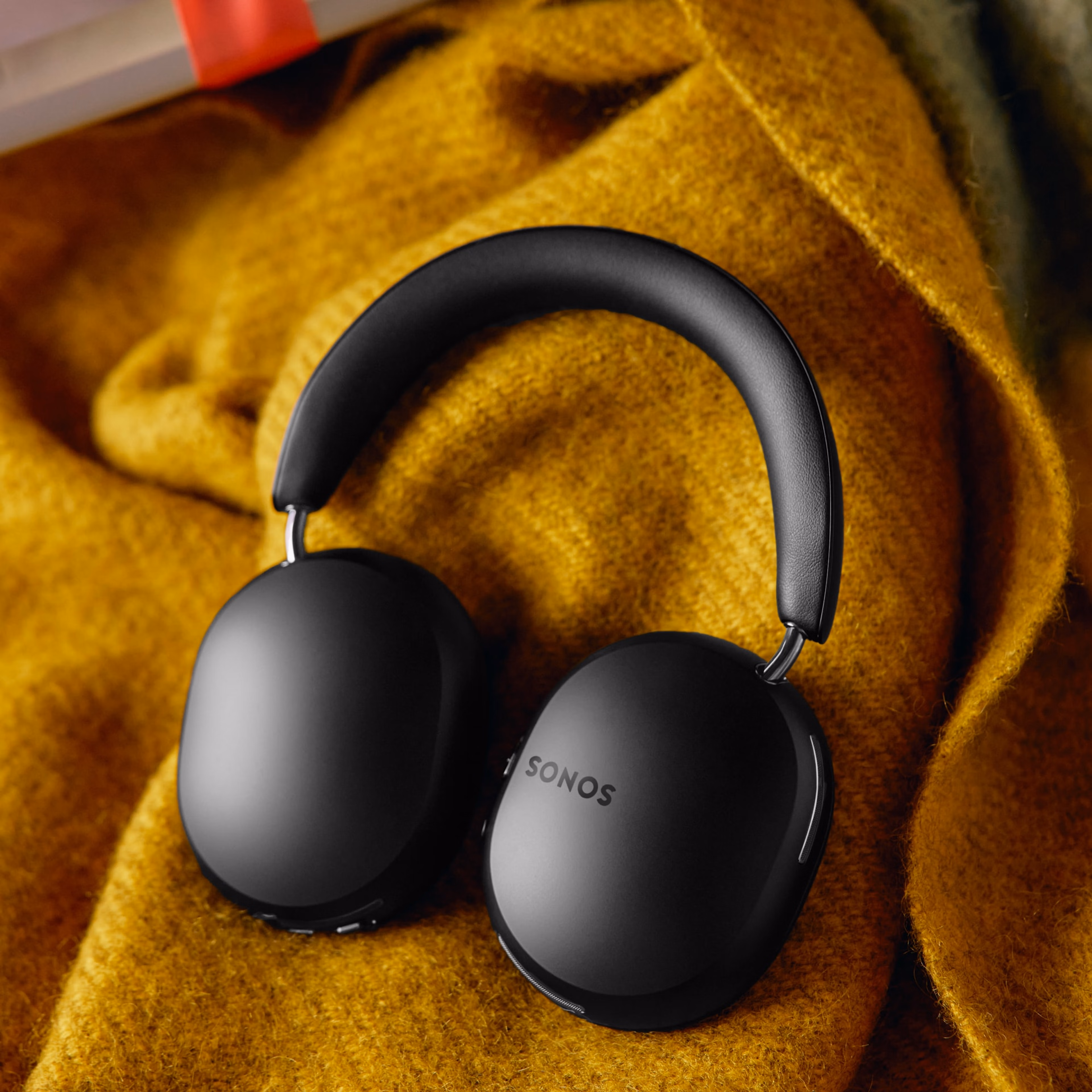 A pair of black Sonos Ace headphones on a yellow blanket