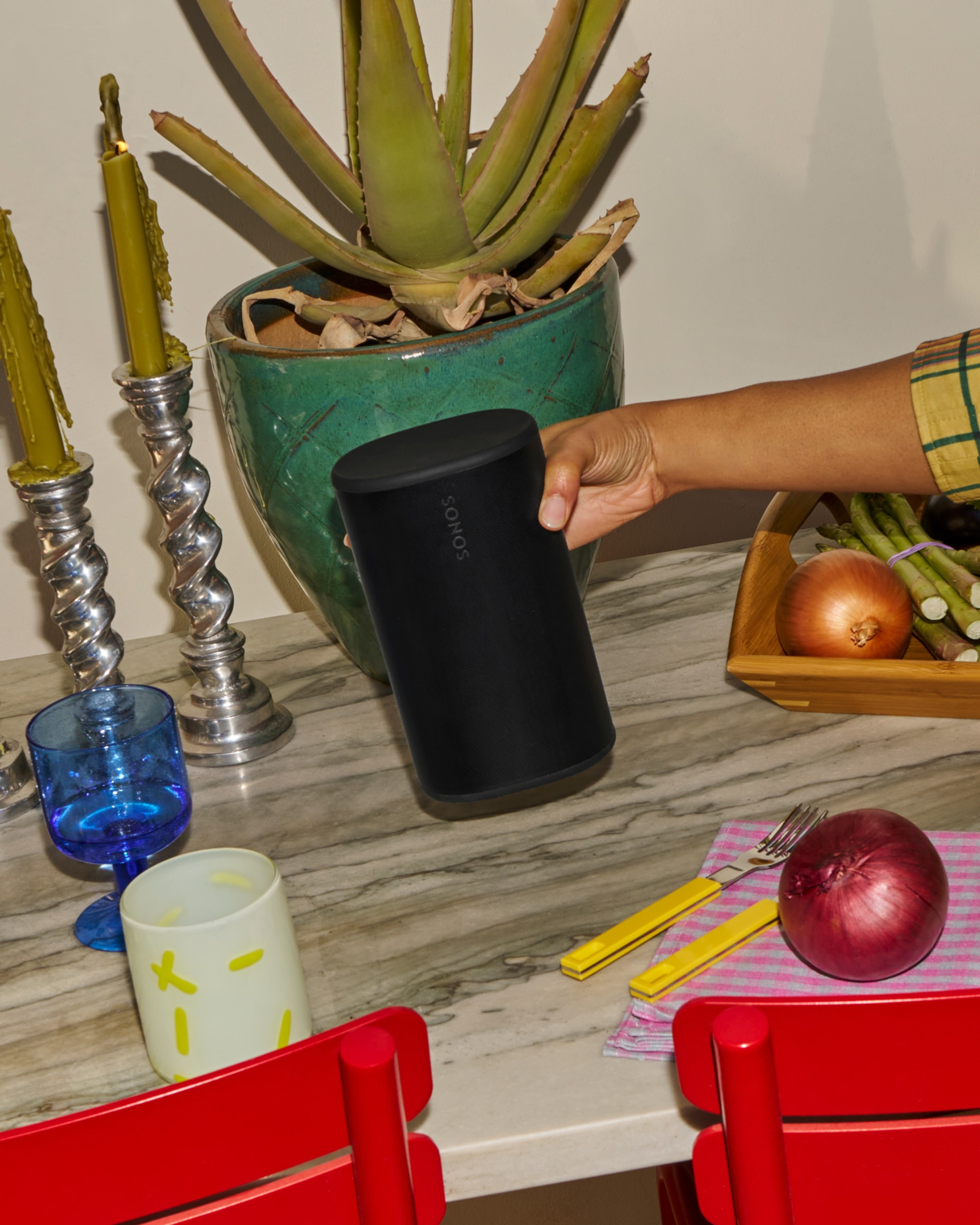 Person setting down a black Sonos Play speaker on a table at a dinner party