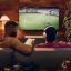 Couple watching soccer on TV with a white Arc Ultra, one is wearing white Sonos Ace headphones, the other is reading