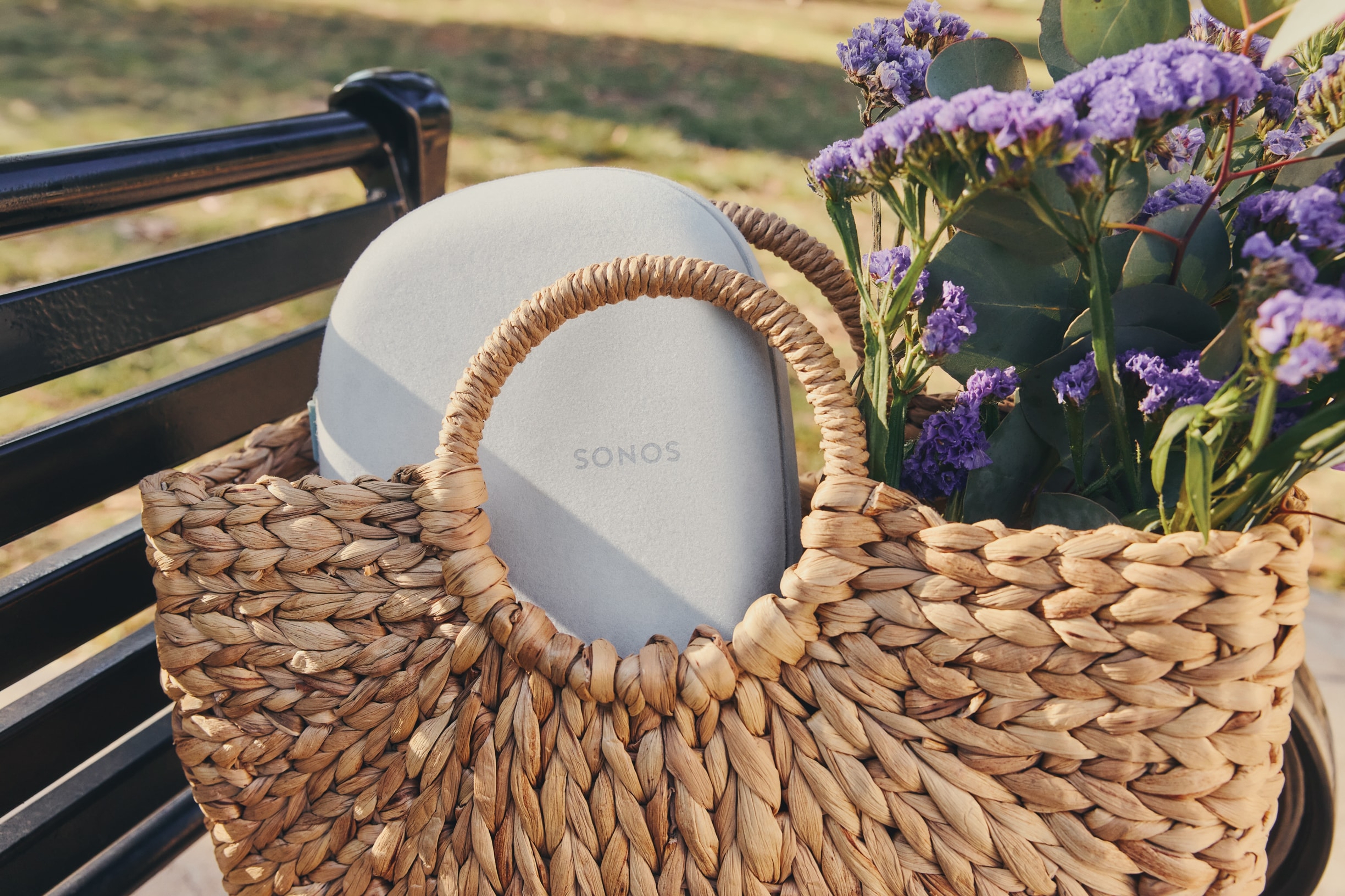 A soft white Sonos Ace case in a woven bag with flowers