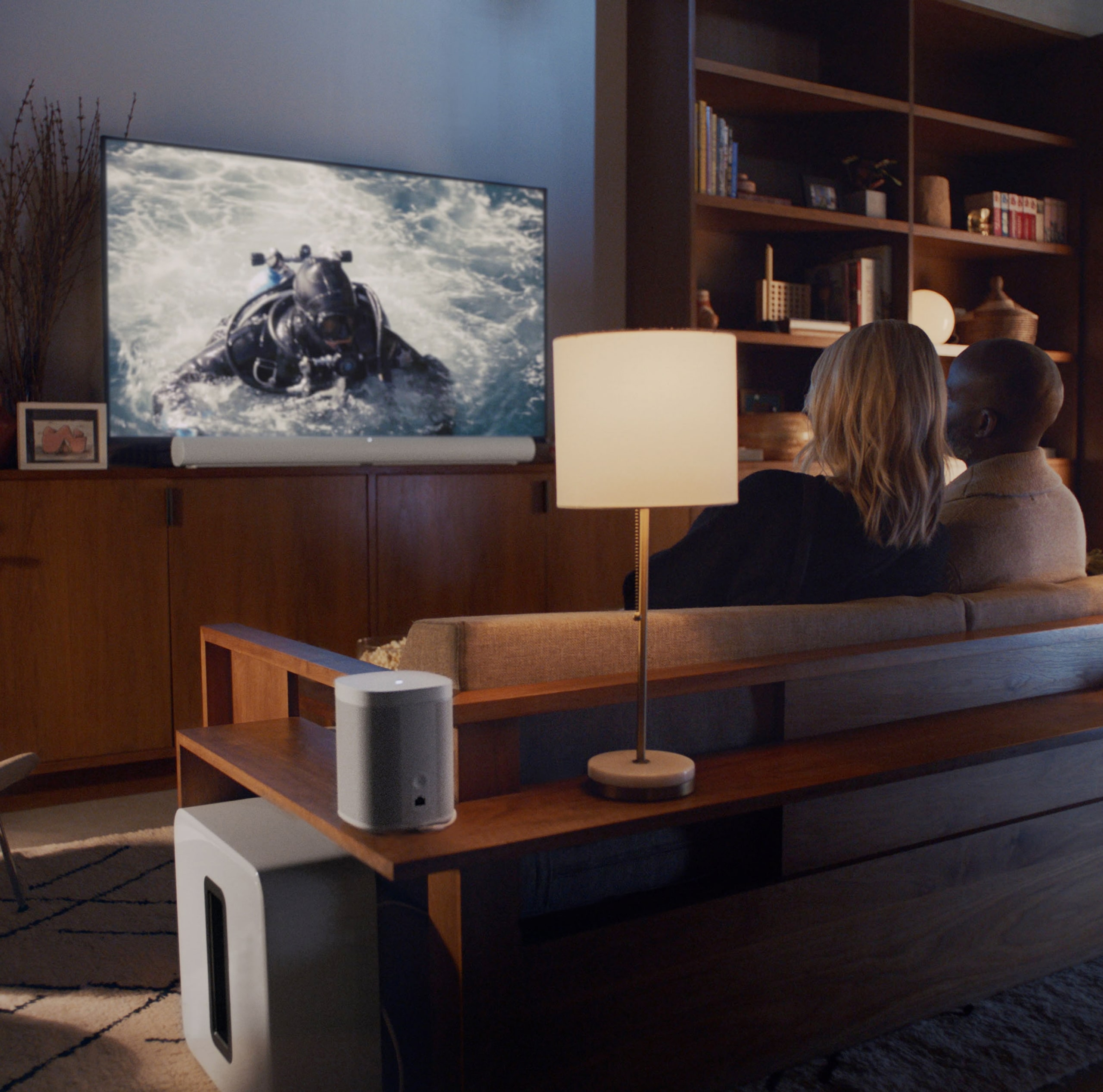 Couple watching TV with white Sonos Arc home theatre system