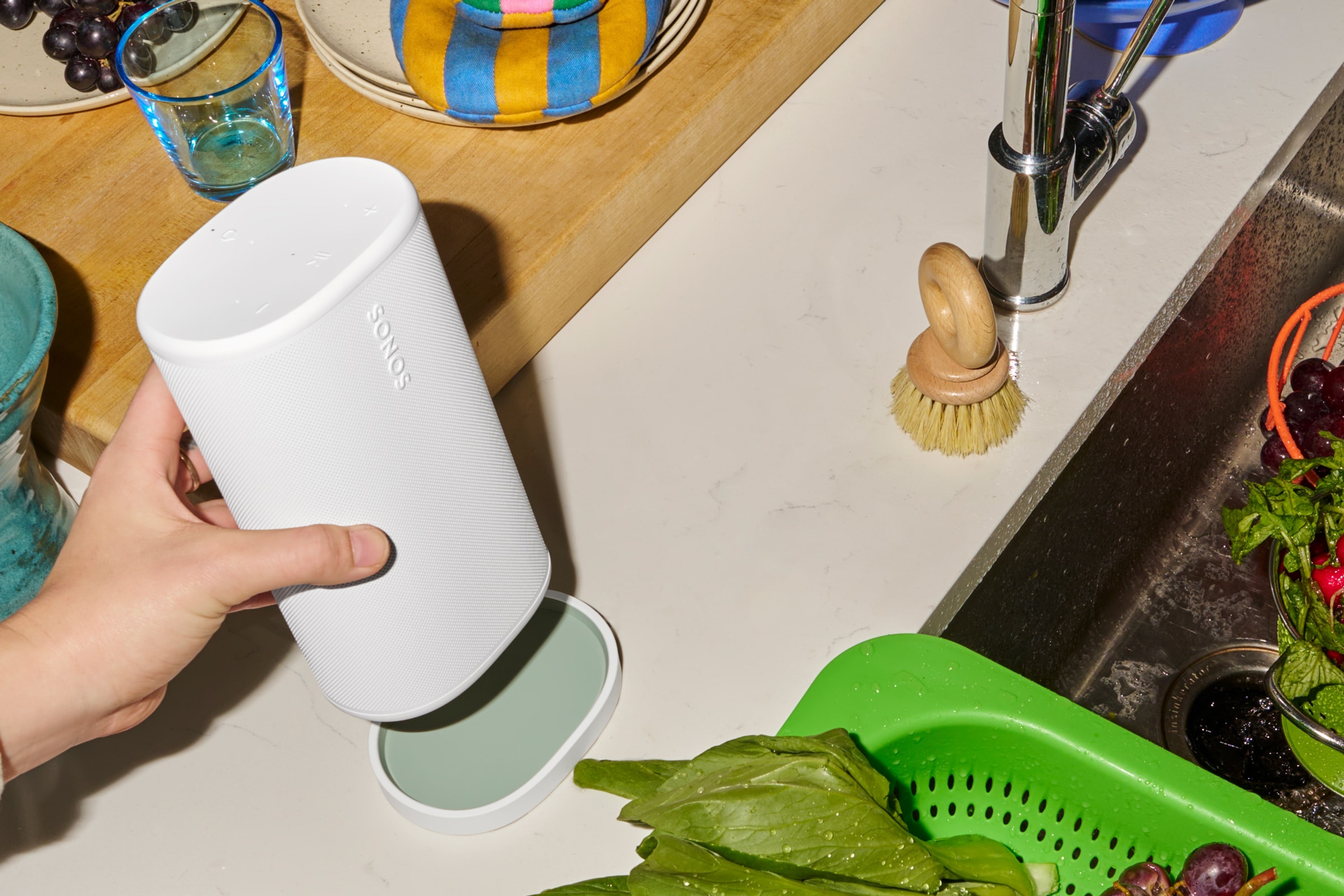 Person placing a white Sonos Play speaker on its matching charging base next to the kitchen sink
