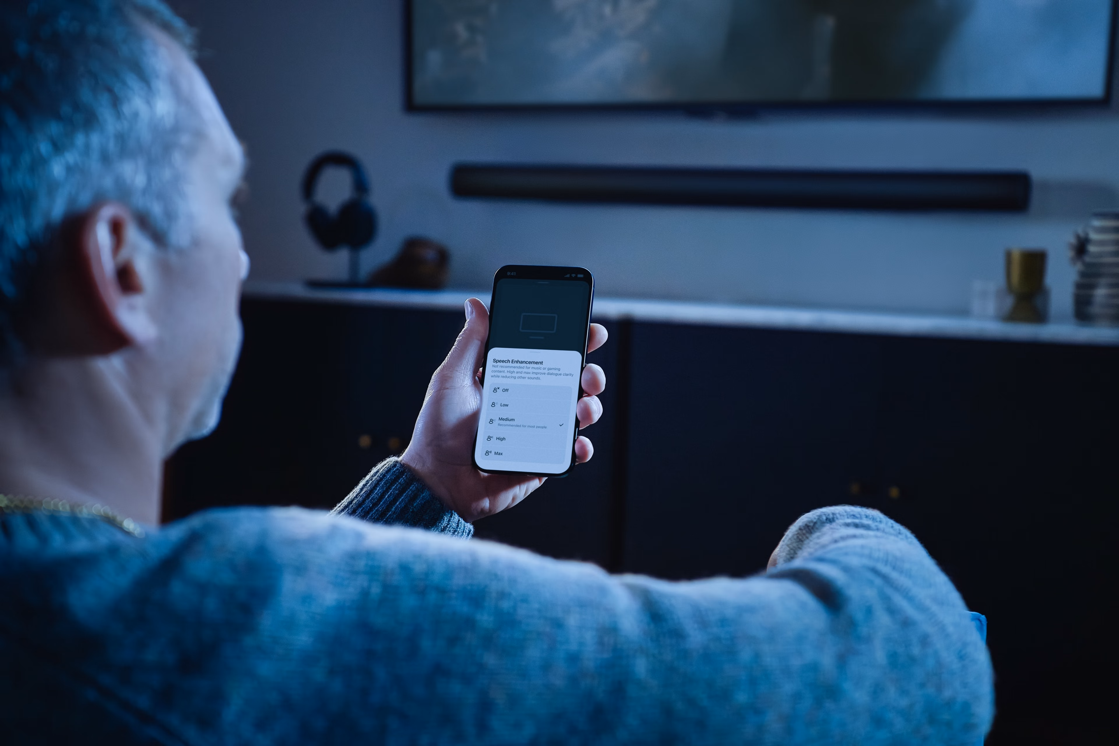 Une personne regardant l'application Sonos sur son smartphone avec une Sonos Arc Ultra en arrière-plan