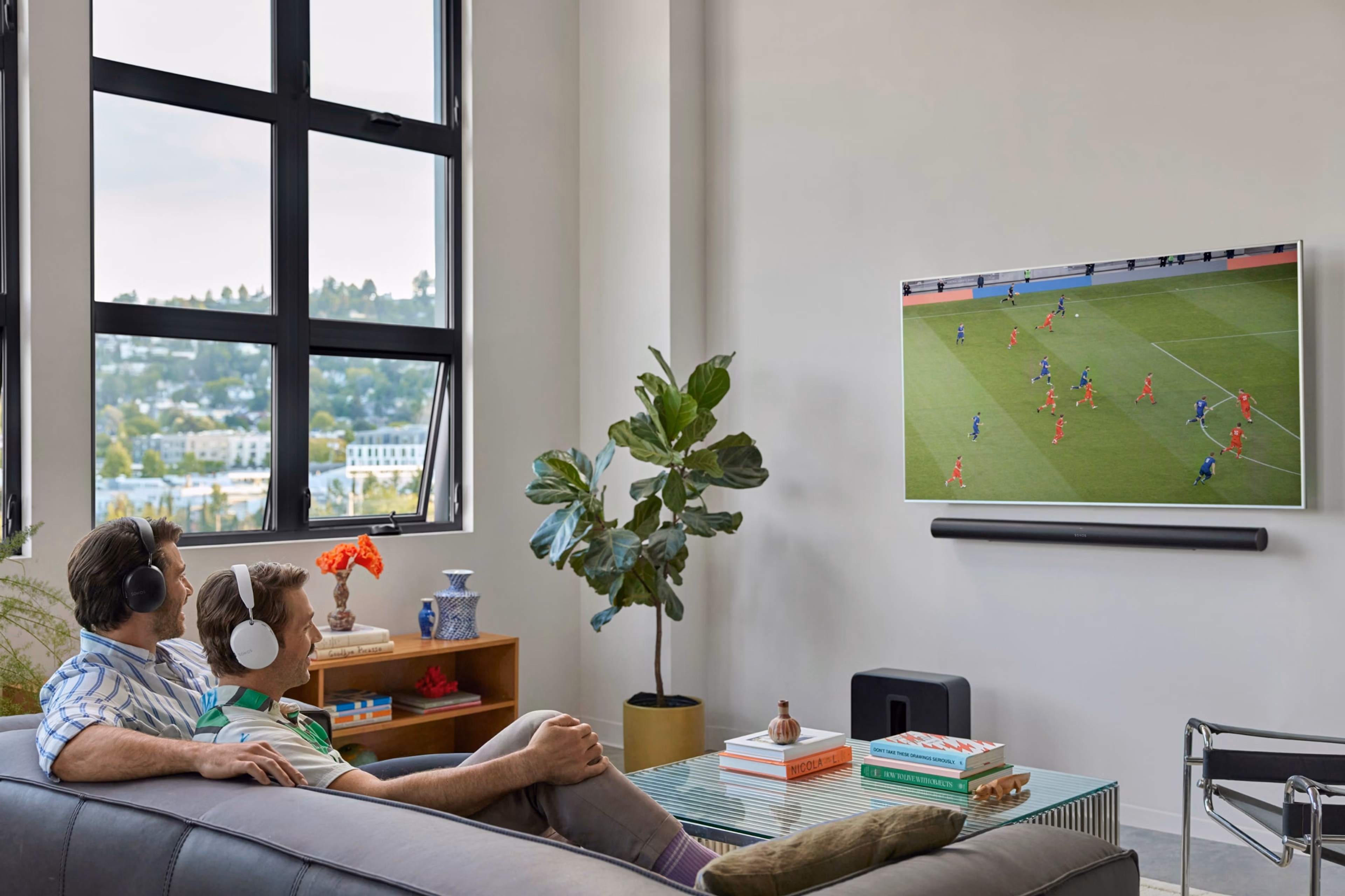 Une famille assise sur un canapé regardant la TV avec une Sonos Arc Ultra noire et un Sonos Sub 4 noir