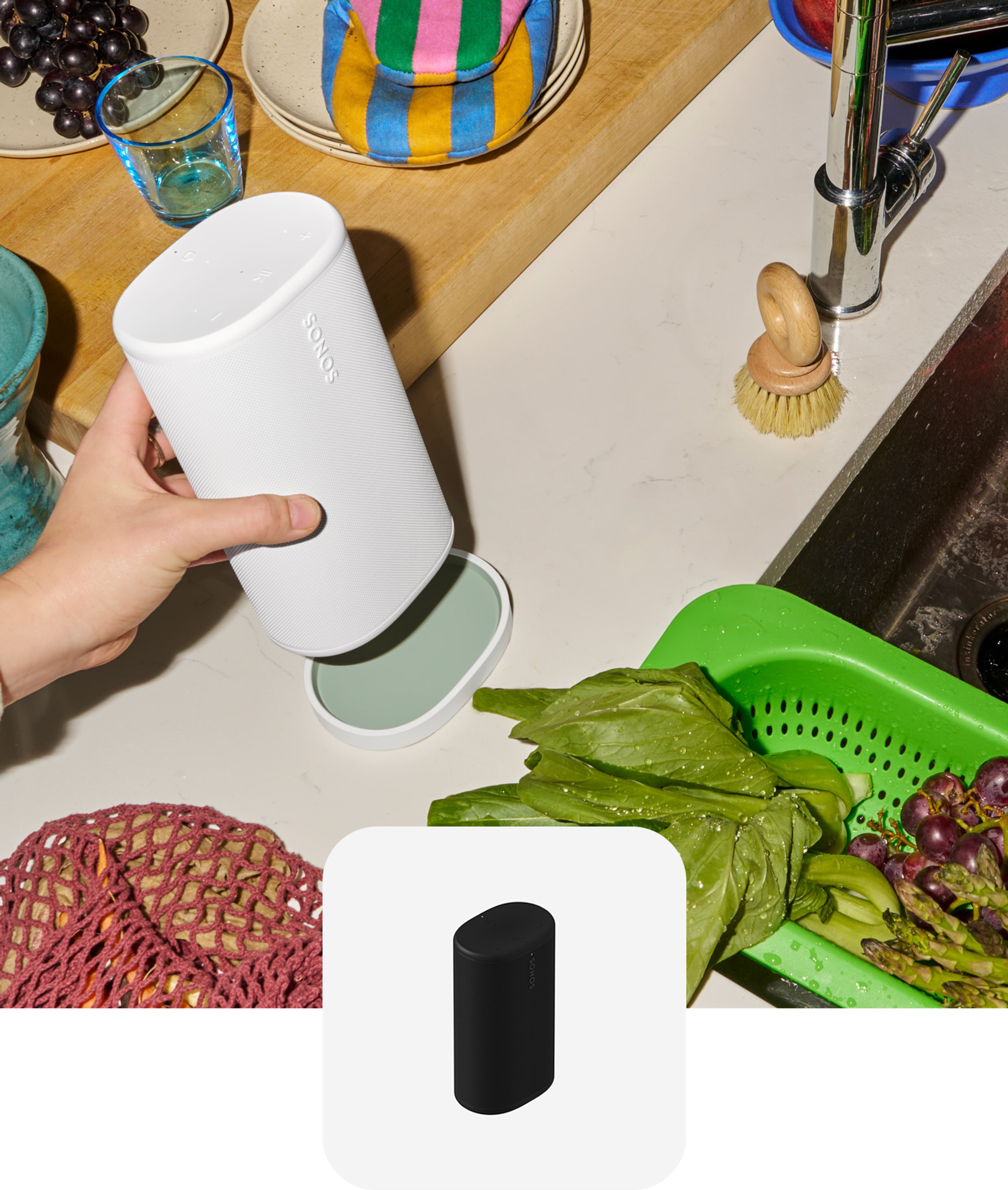 Hand placing a white Sonos Play on the charging base next to a kitchen sink