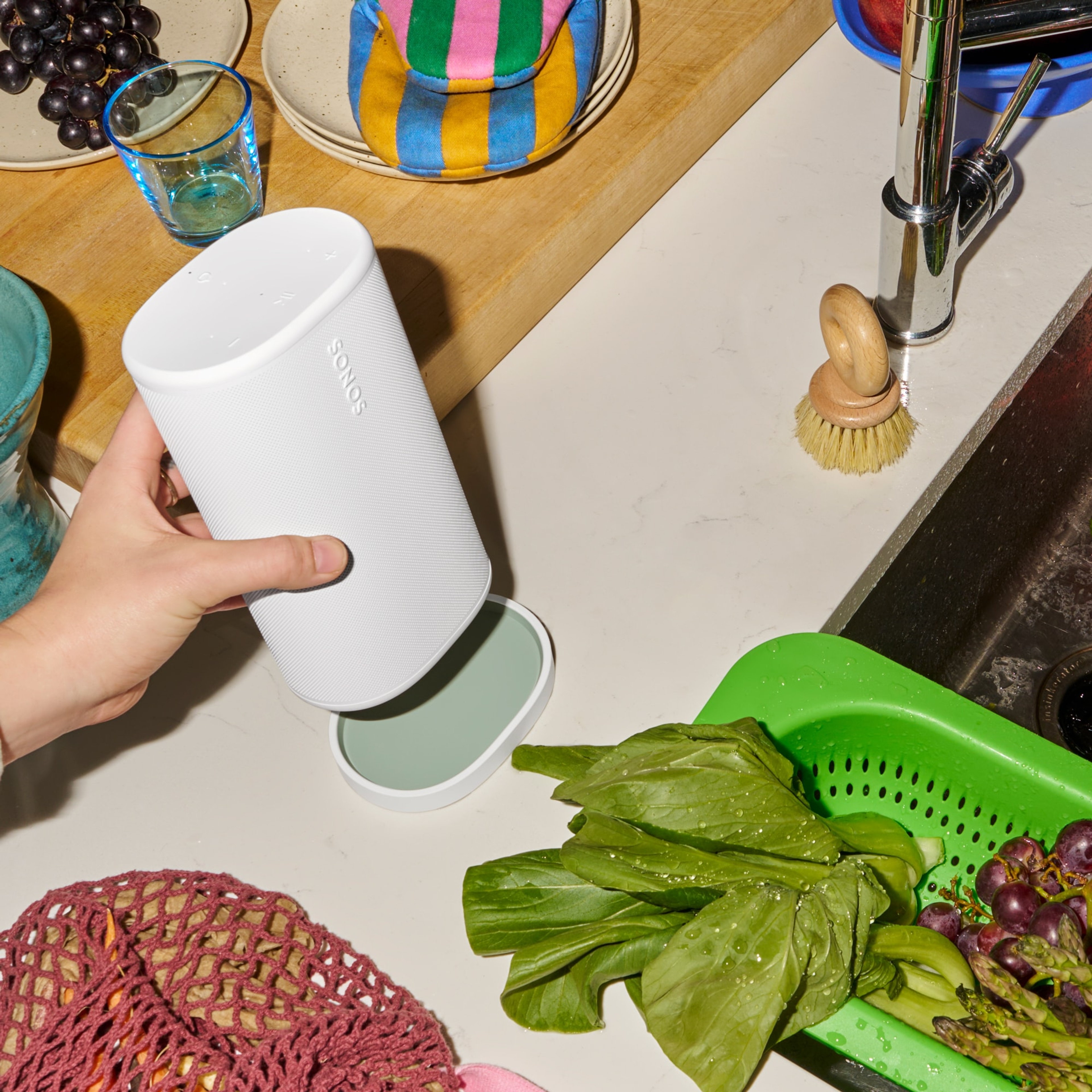 Persoon die een witte Sonos Play-speaker op een bijpassende oplader plaatst naast een gootsteen