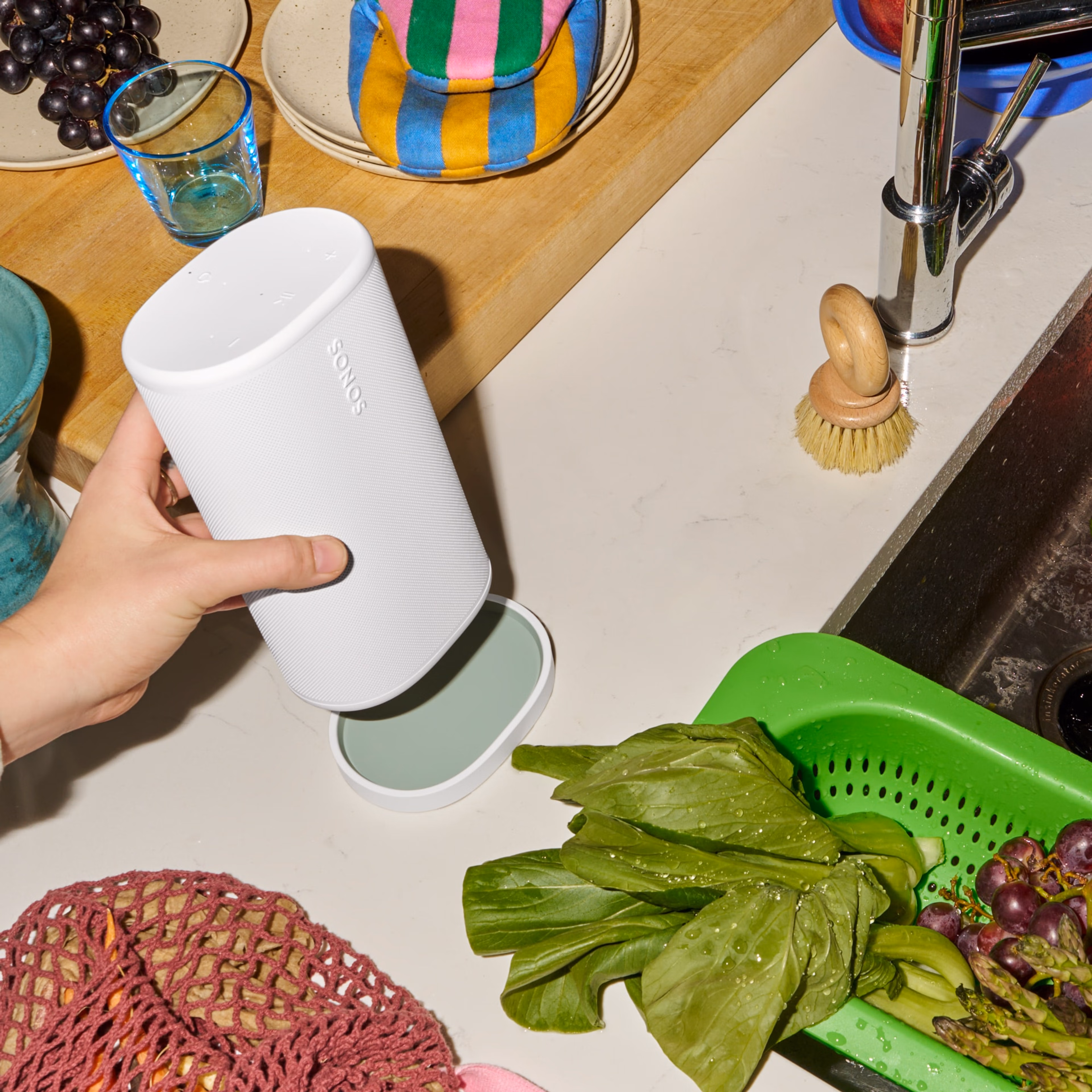 Persoon die een witte Sonos Play-speaker op een bijpassende oplader plaatst naast een gootsteen