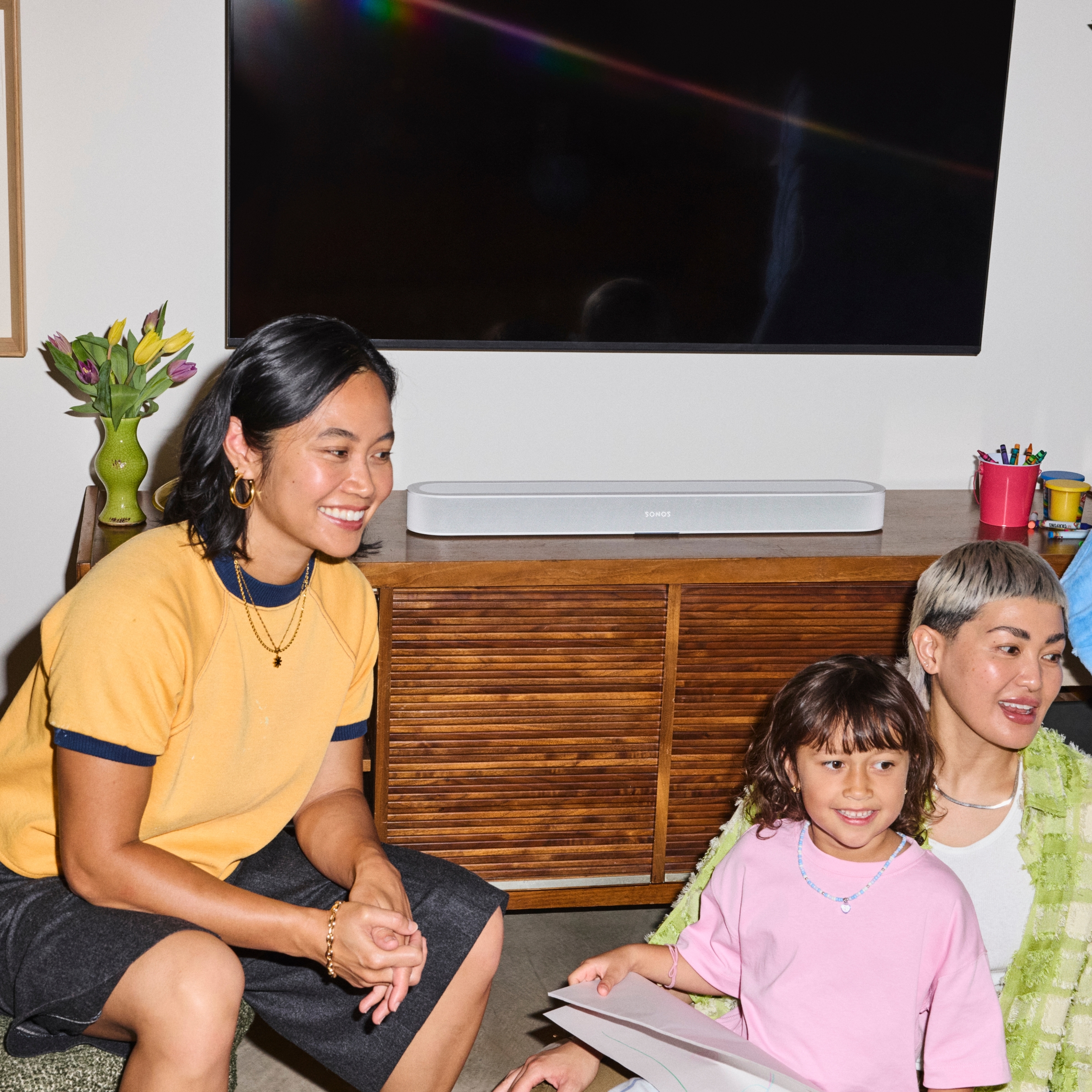 Family sitting together in front of a wooden TV stand with a Sonos Beam Ultra soundbar