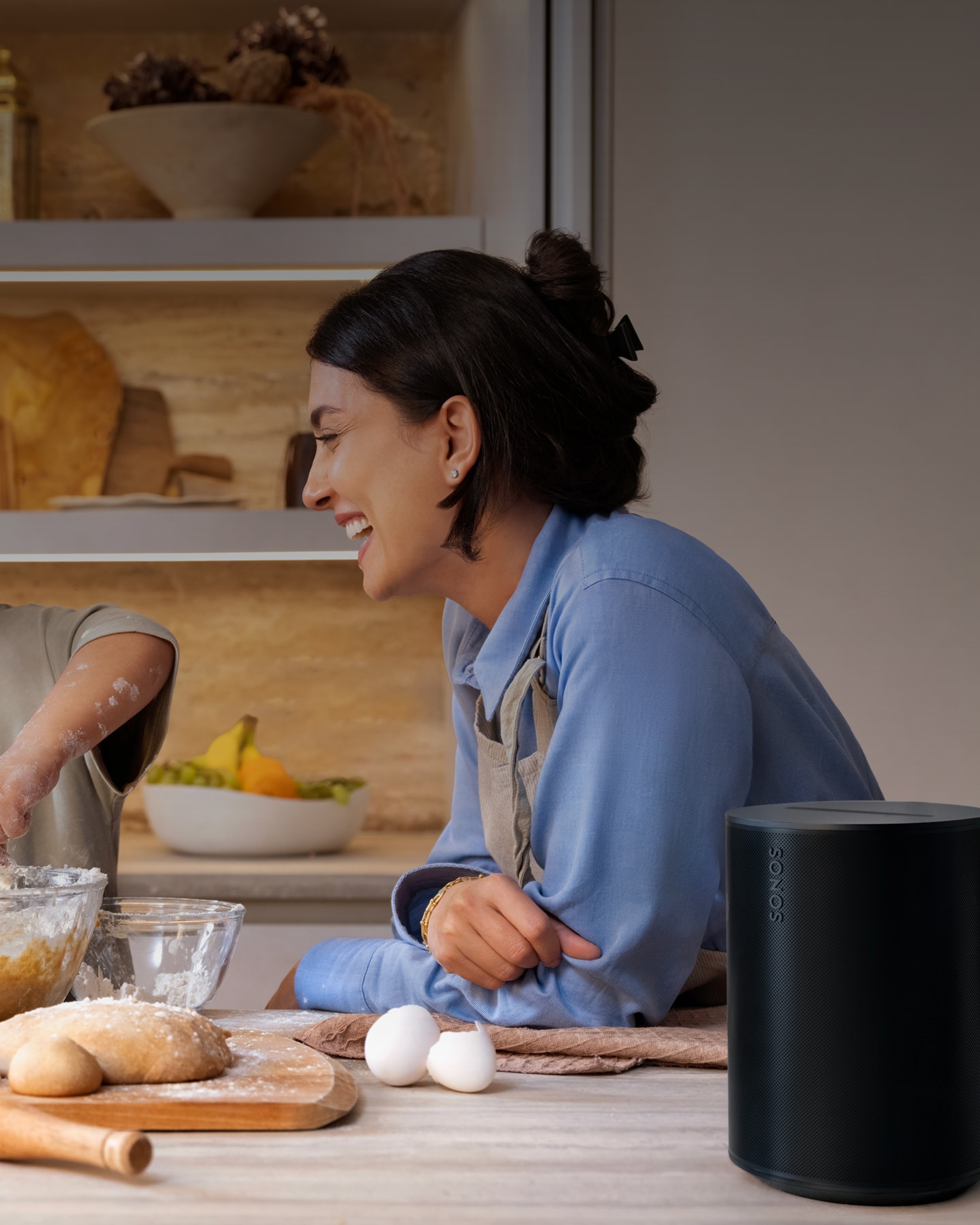 A mother and son baking together in the kitchen listening to music on a black Sonos Era 100 speaker