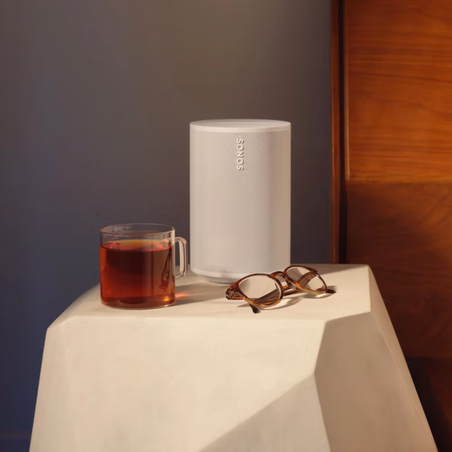 A white Era 100 speaker on a nightstand next to a bed