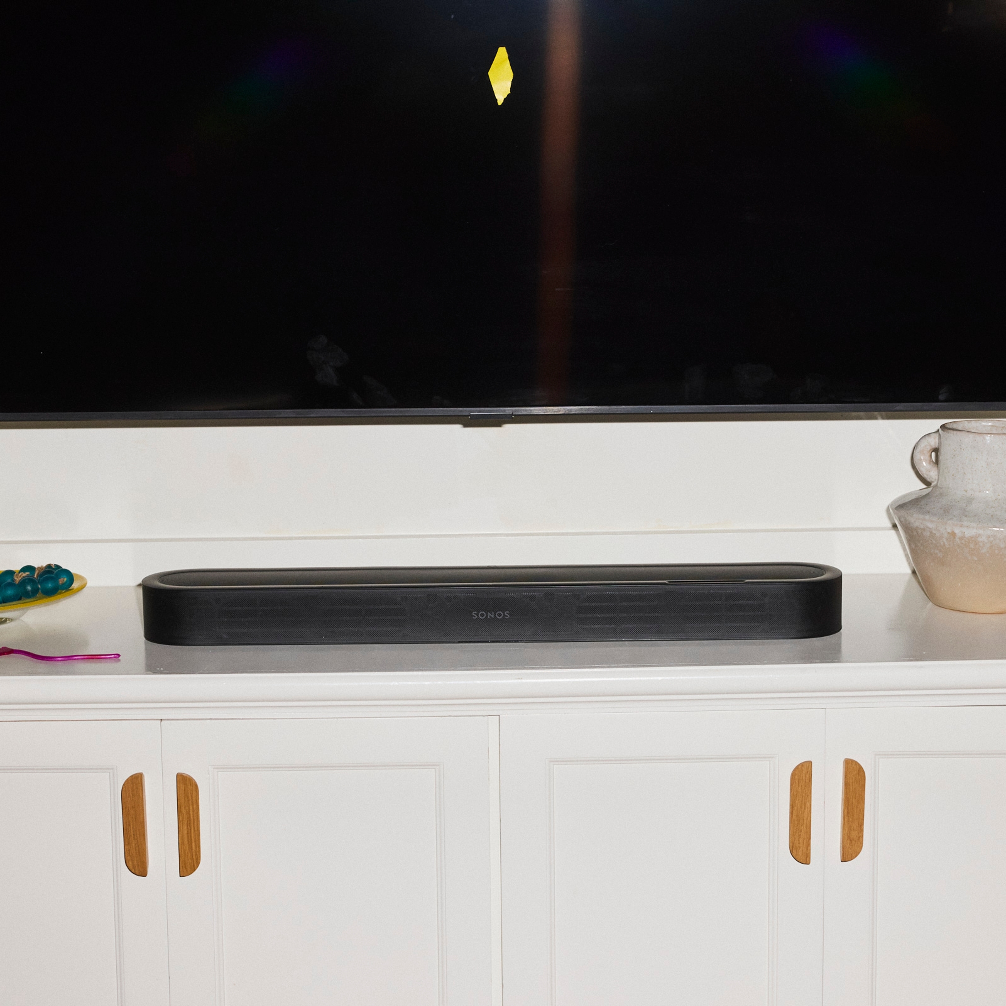 A black Sonos Beam Ultra soundbar on a white cabinet with wooden handles