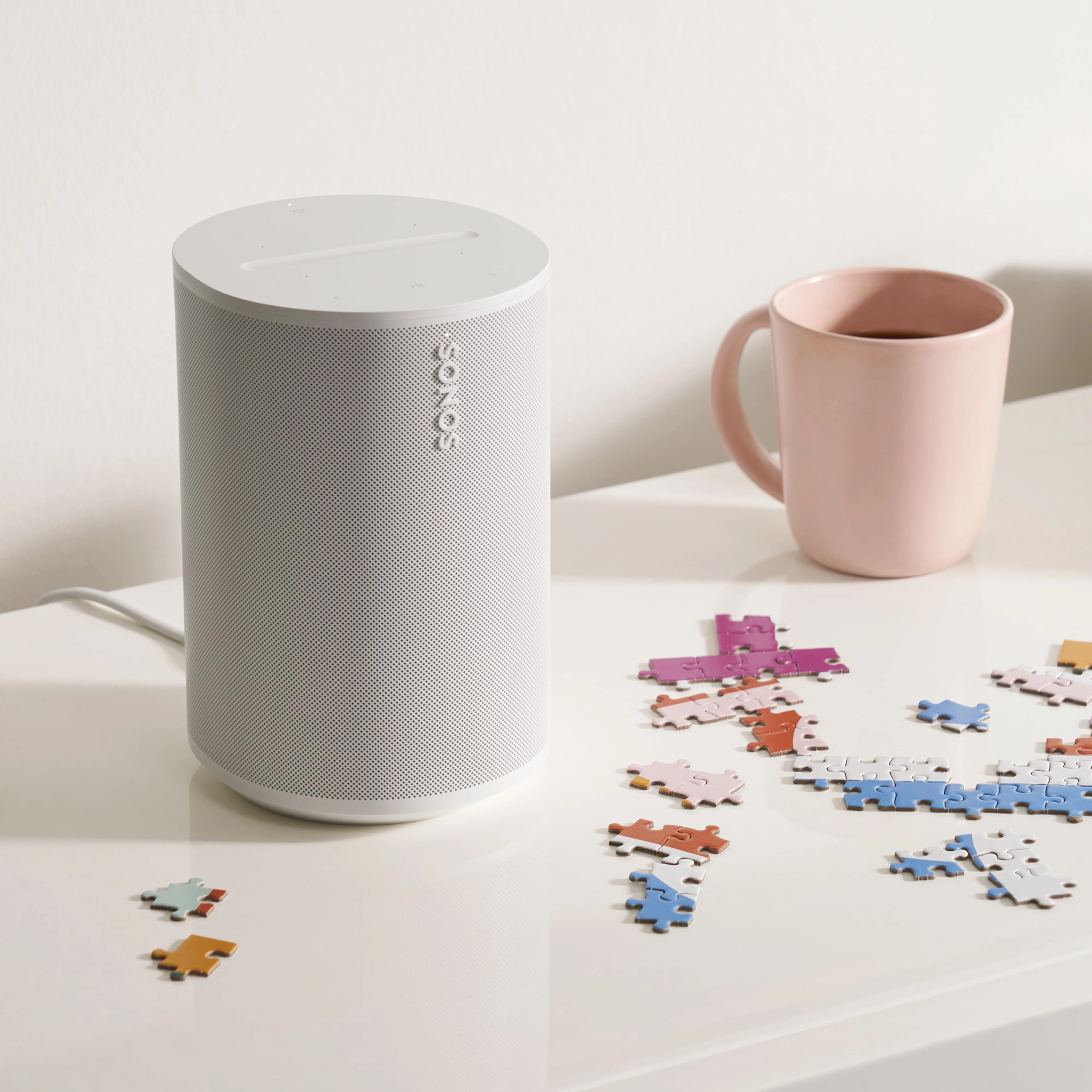 A white Era 100 speaker providing immersive sound while doing a puzzle and sipping your coffee