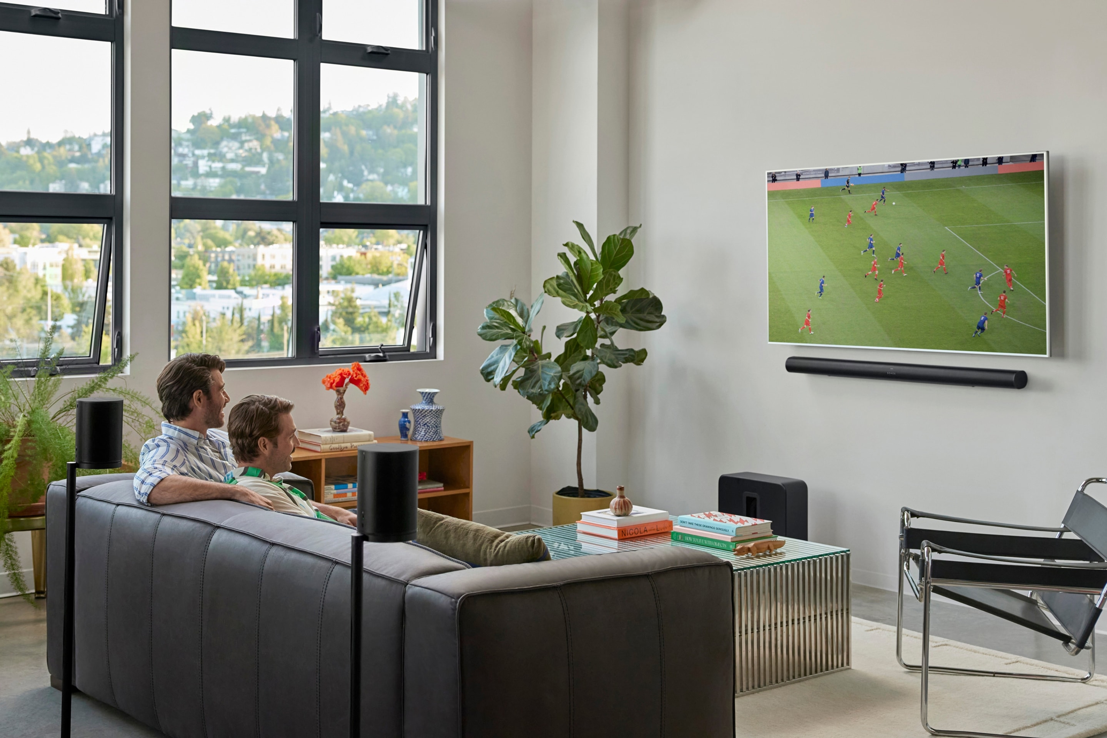A couple on the couch watching a football match with a Sonos Arc Ultra, Sub 4, and Era 100 speakers home theater setup
