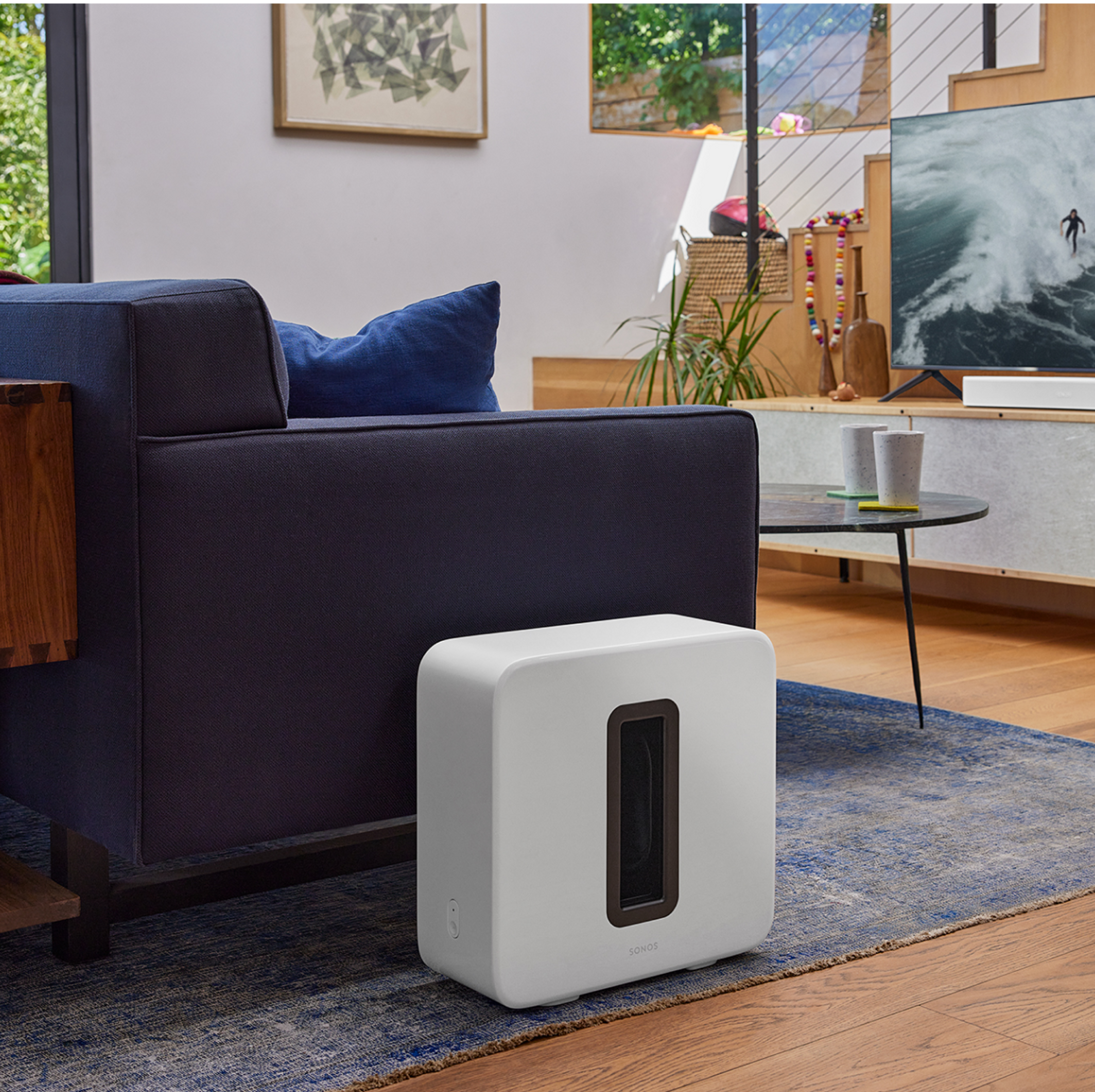 Ein Sonos Sub in Weiß als Teil eines Heimkinos neben einer Couch in einem Wohnzimmer