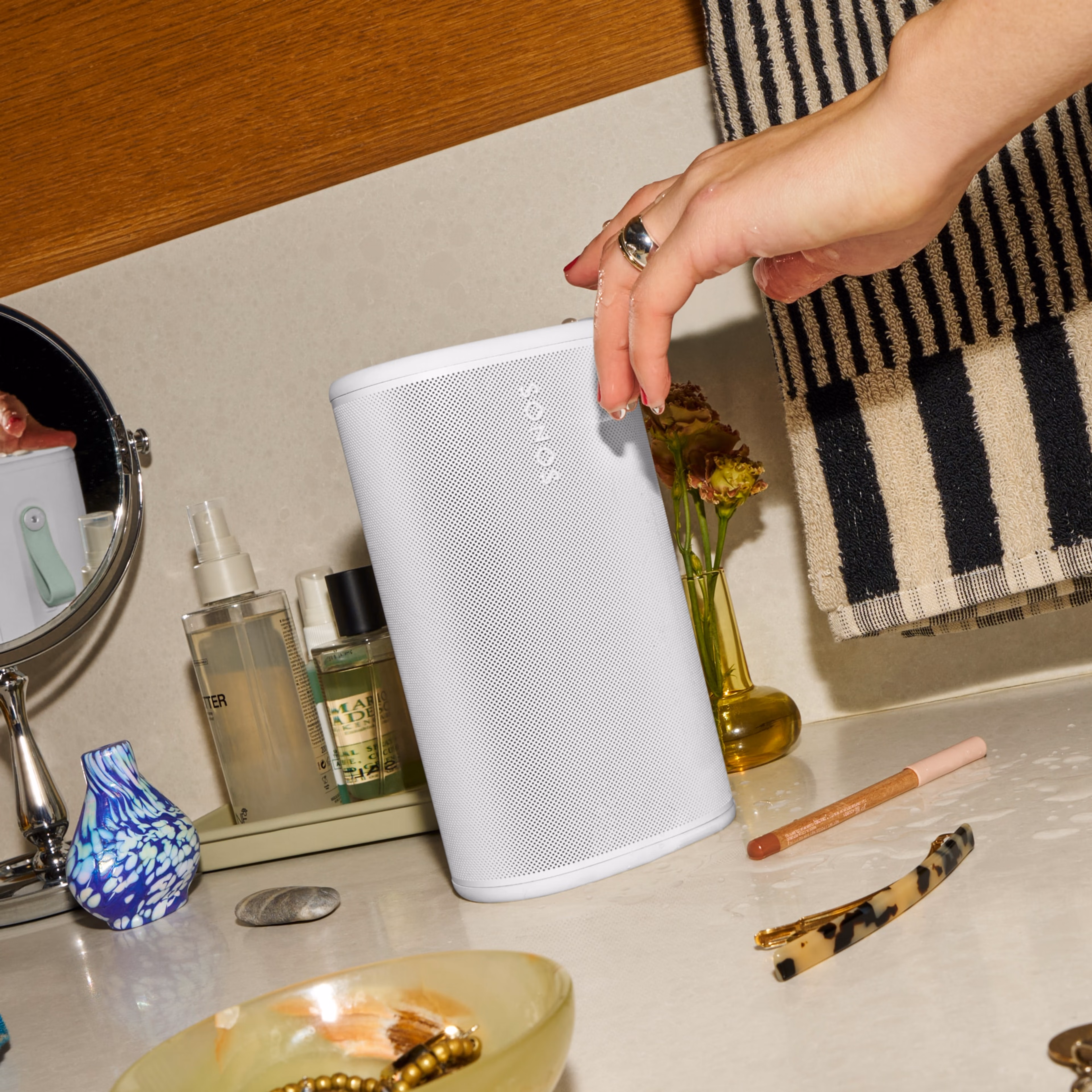 棚に置かれたSonos Playスピーカー(ホワイト)の上面にあるコントロール部分を操作している人