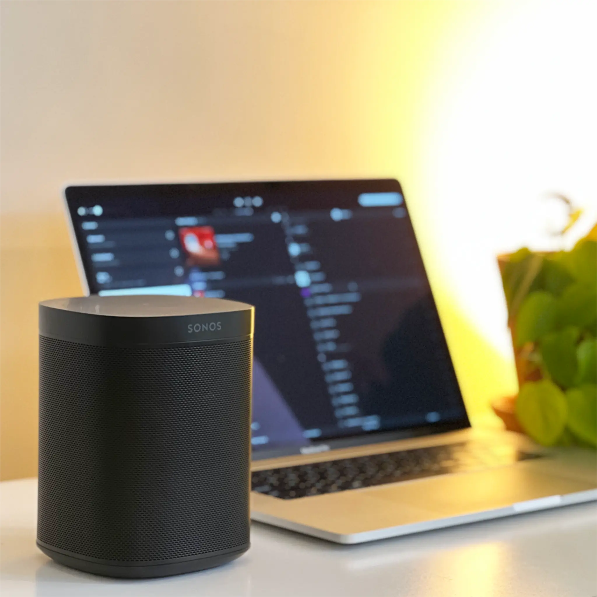 A laptop running the Sonos app for macOS and Windows, with a Sonos One in the foreground
