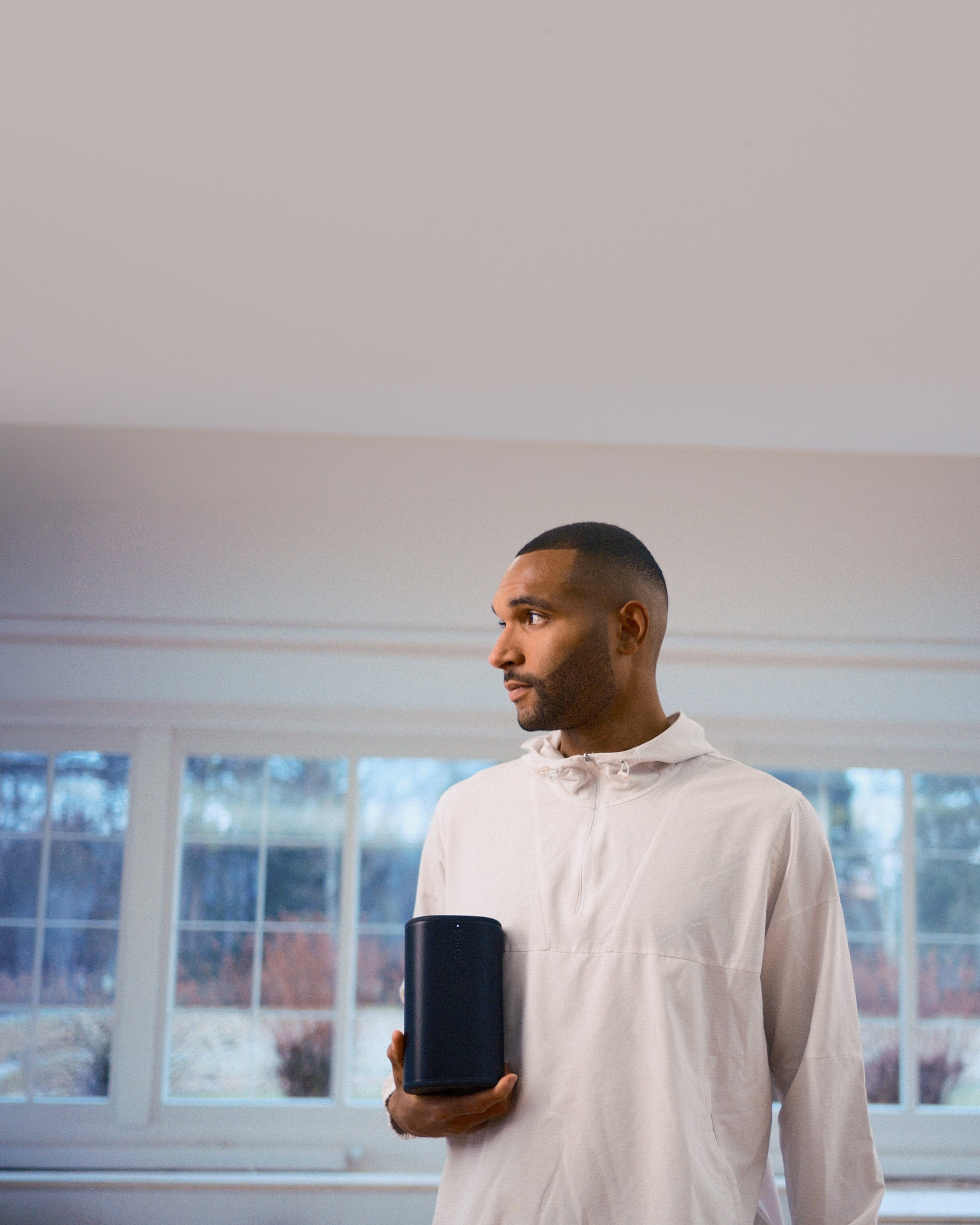 German footballer Jonathan Tah holding a black Sonos Play speaker in his home