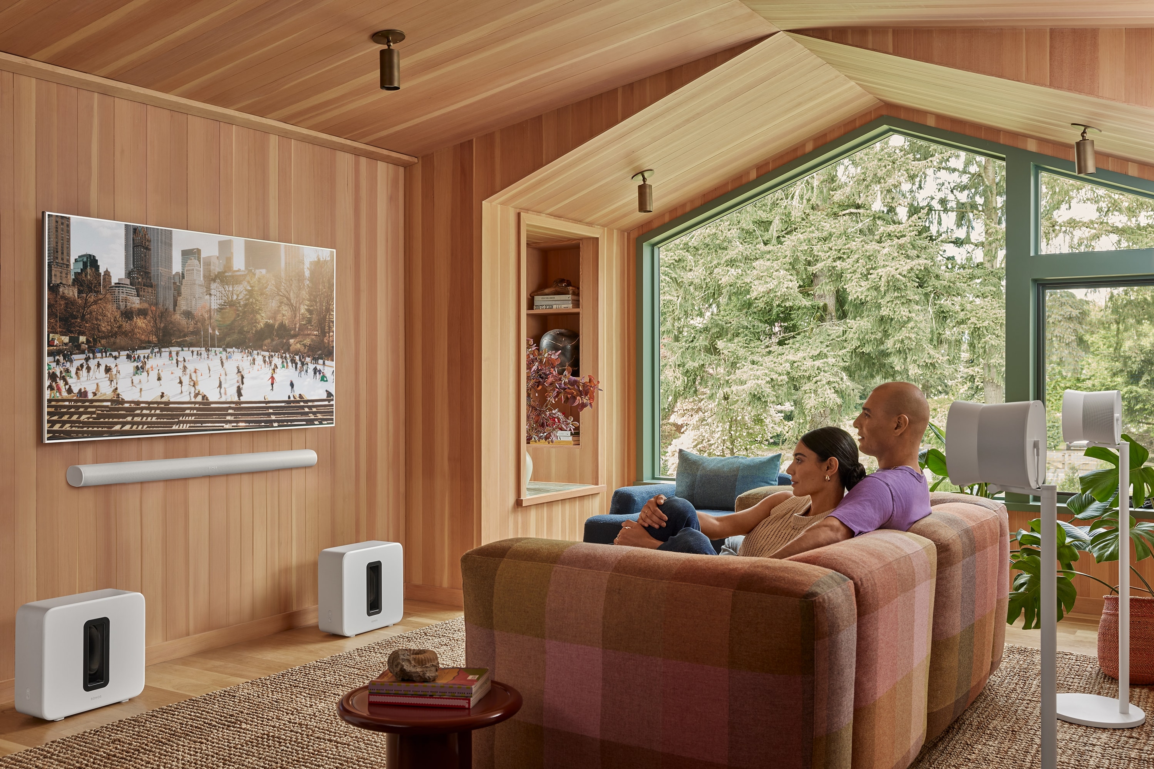 Couple watching skaters on tv with a white Arc Ultra, pair of Sub 4, and pair of Era 300