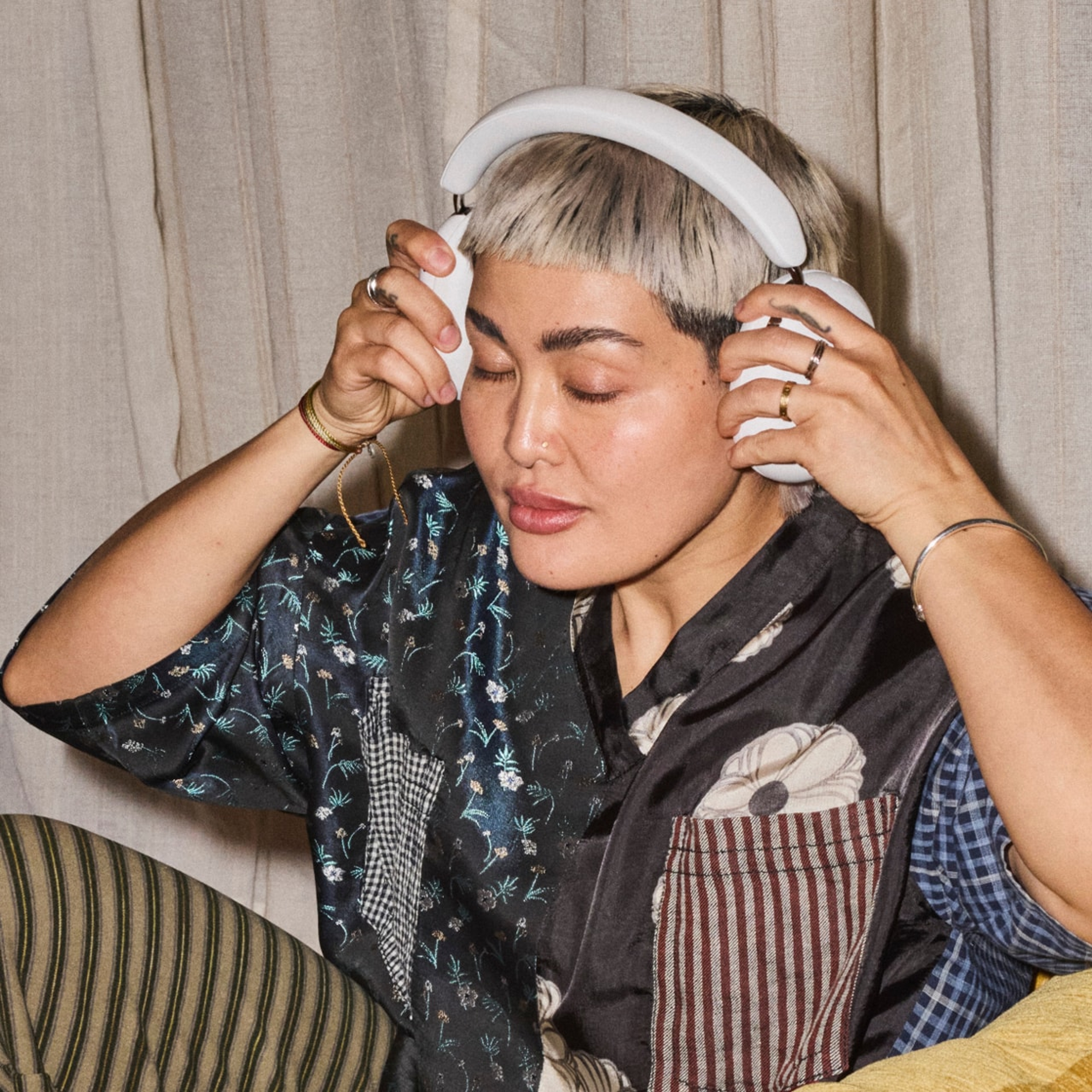 Person sitting on a couch with their eyes closed listening to music on a pair of white Sonos Ace Ultra headphones
