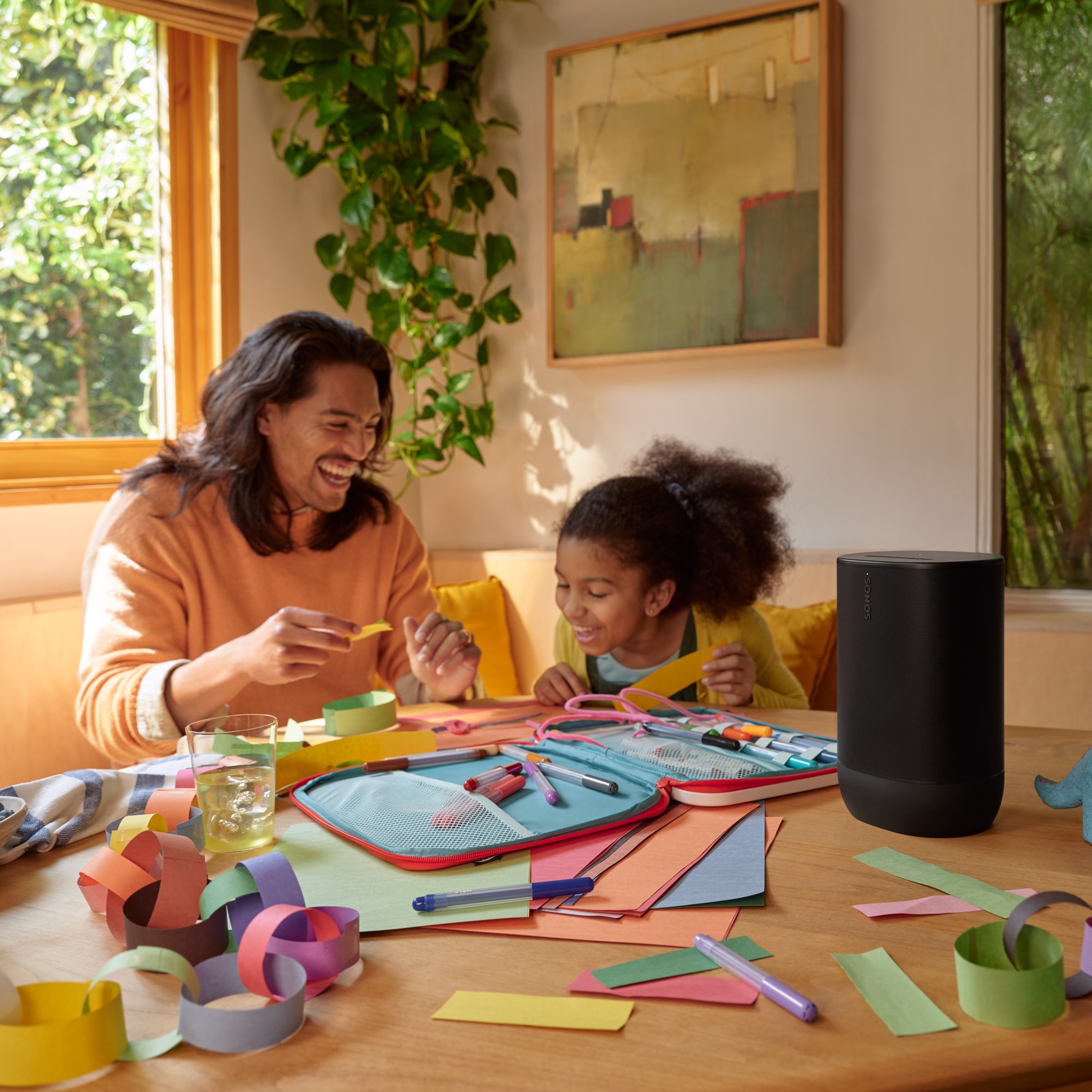Photo d'un père et de sa fille à la table de la cuisine en train de bricoler tout en écoutant de la musique diffusée par un Sonos Move 2 noir