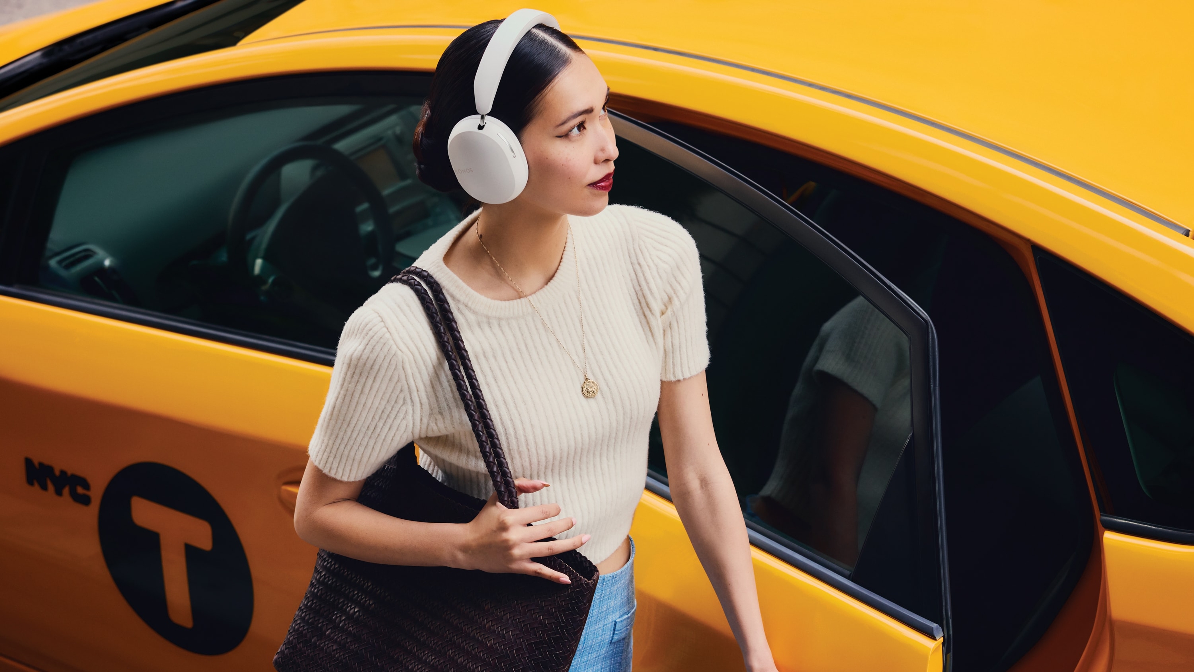 Una persona que lleva puestos audífonos Sonos Ace en color soft white junto a un taxi