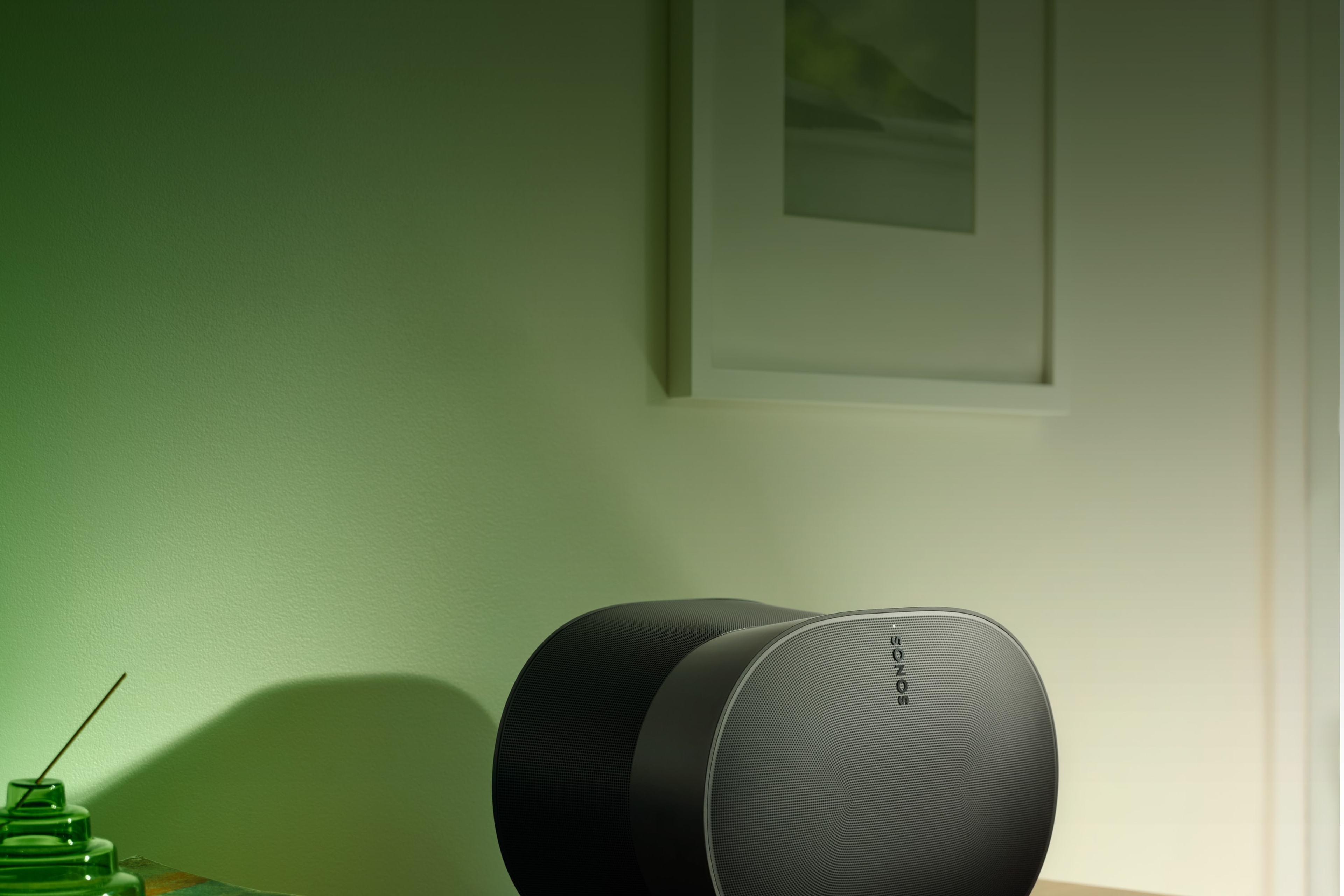 Une enceinte Sonos Era 300 noire sur une table, éclairée par une ampoule verte Philips Hue