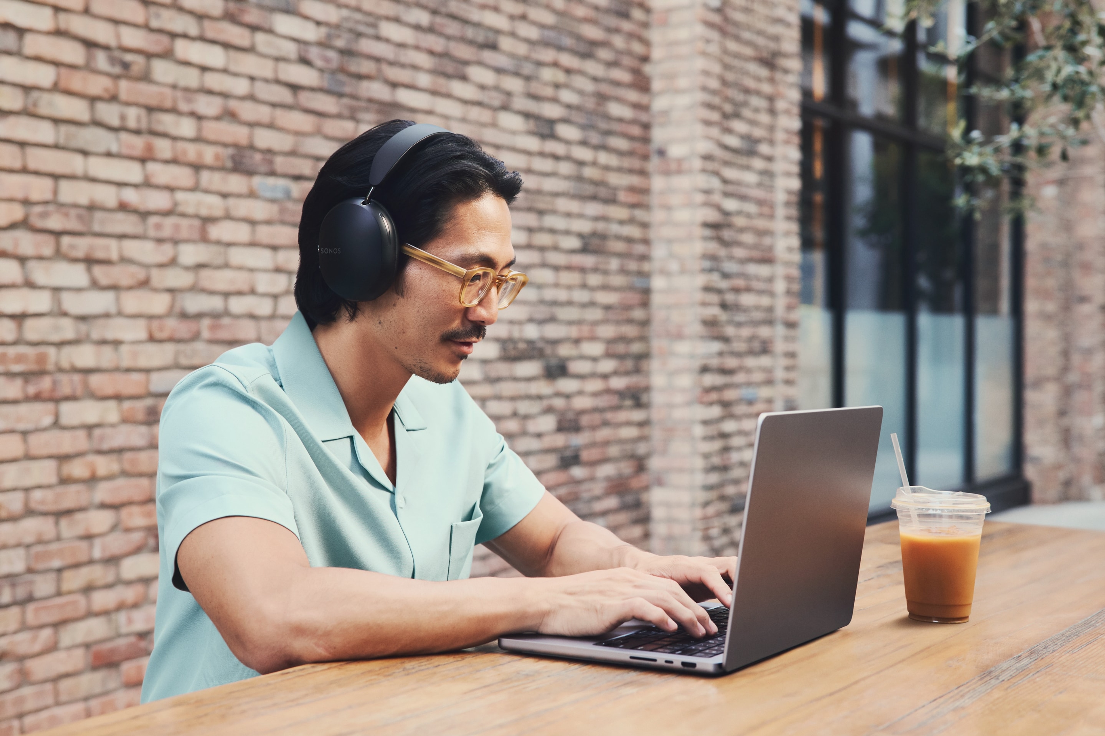 Une personne devant un café portant un Sonos Ace noir et travaillant sur un ordinateur portable