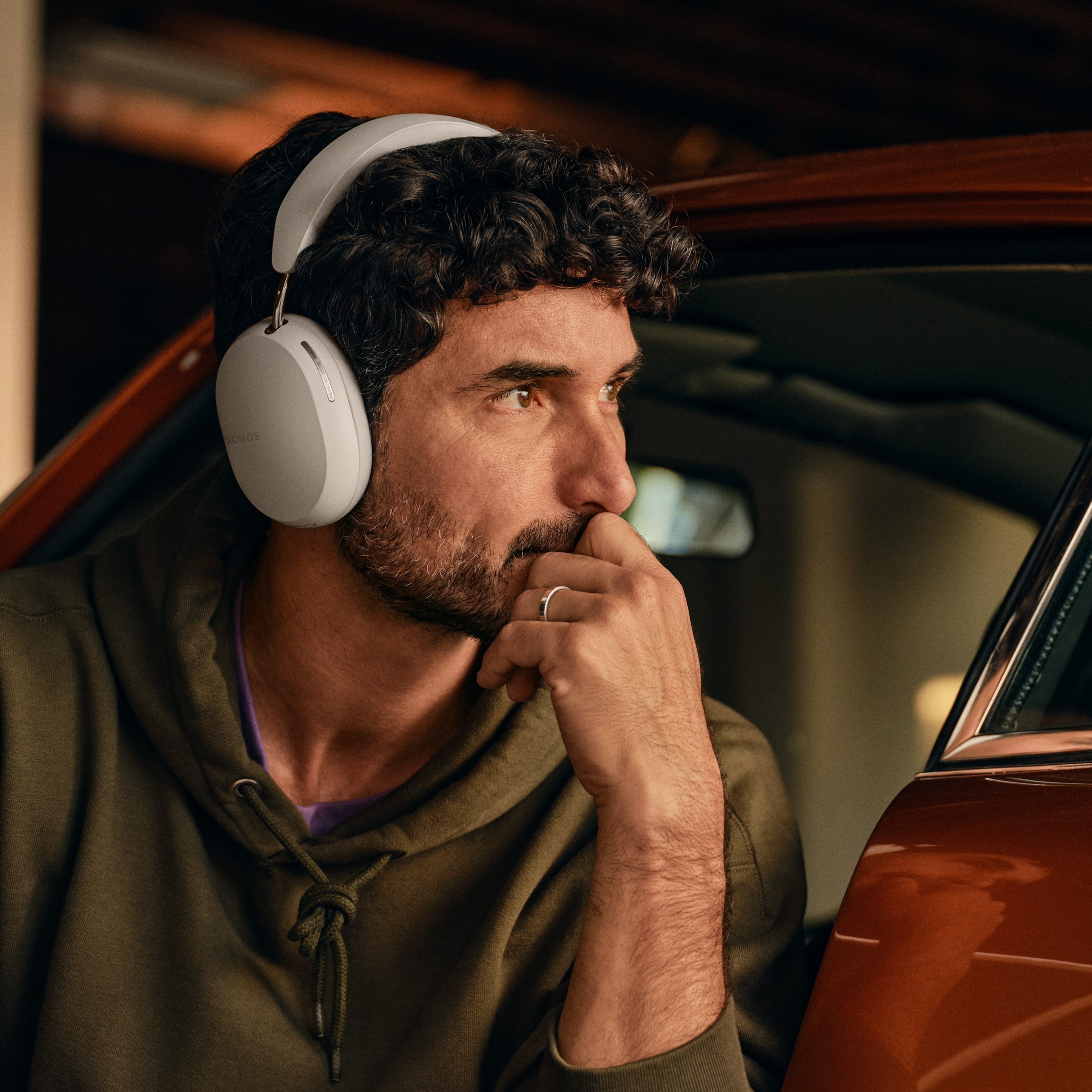 Un homme en train de réparer une voiture porte un casque audio Sonos Ace couleur Soft White