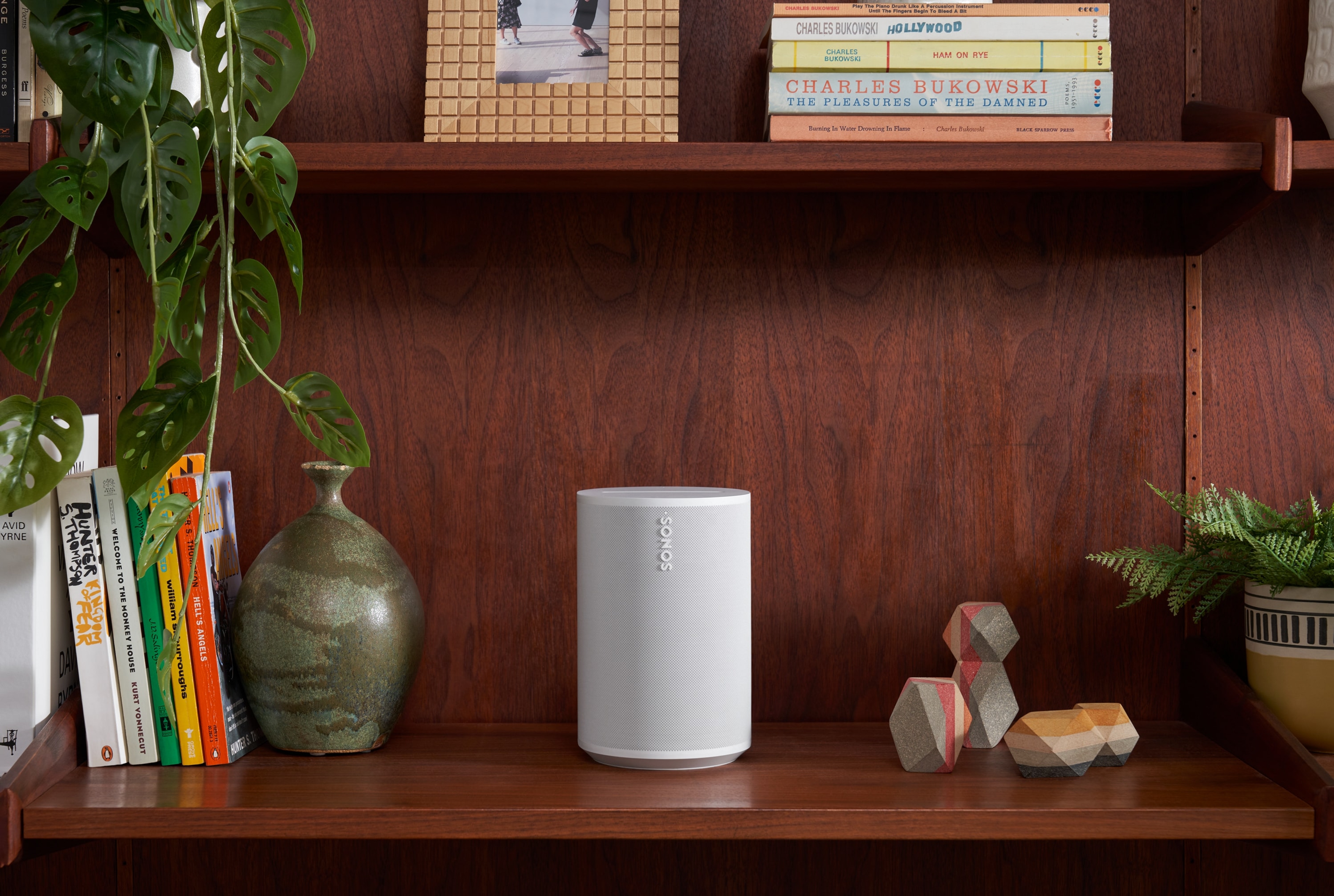 A white Sonos Era 100 on a dark bookshelf