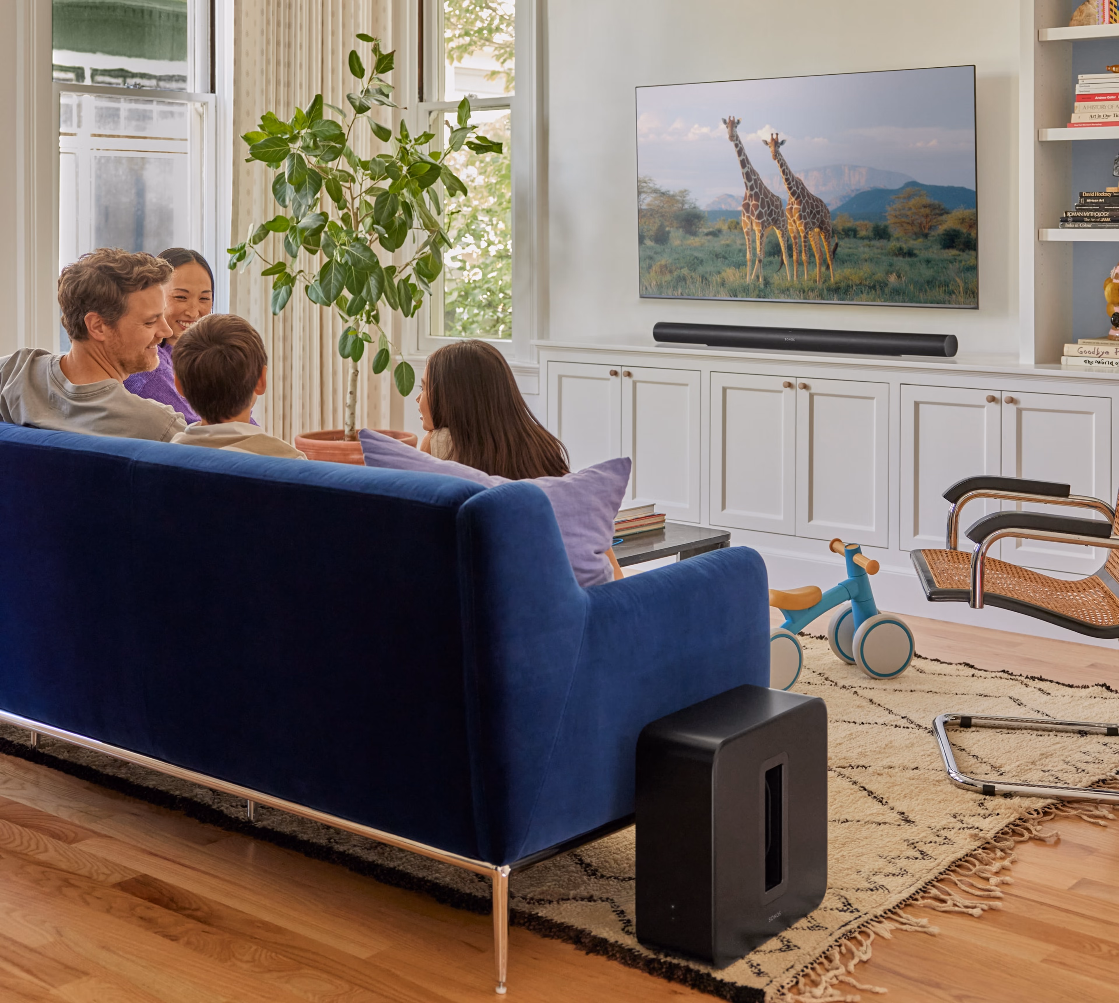 Family seated on a couch watching TV with a black Arc Ultra and a black Sub 4