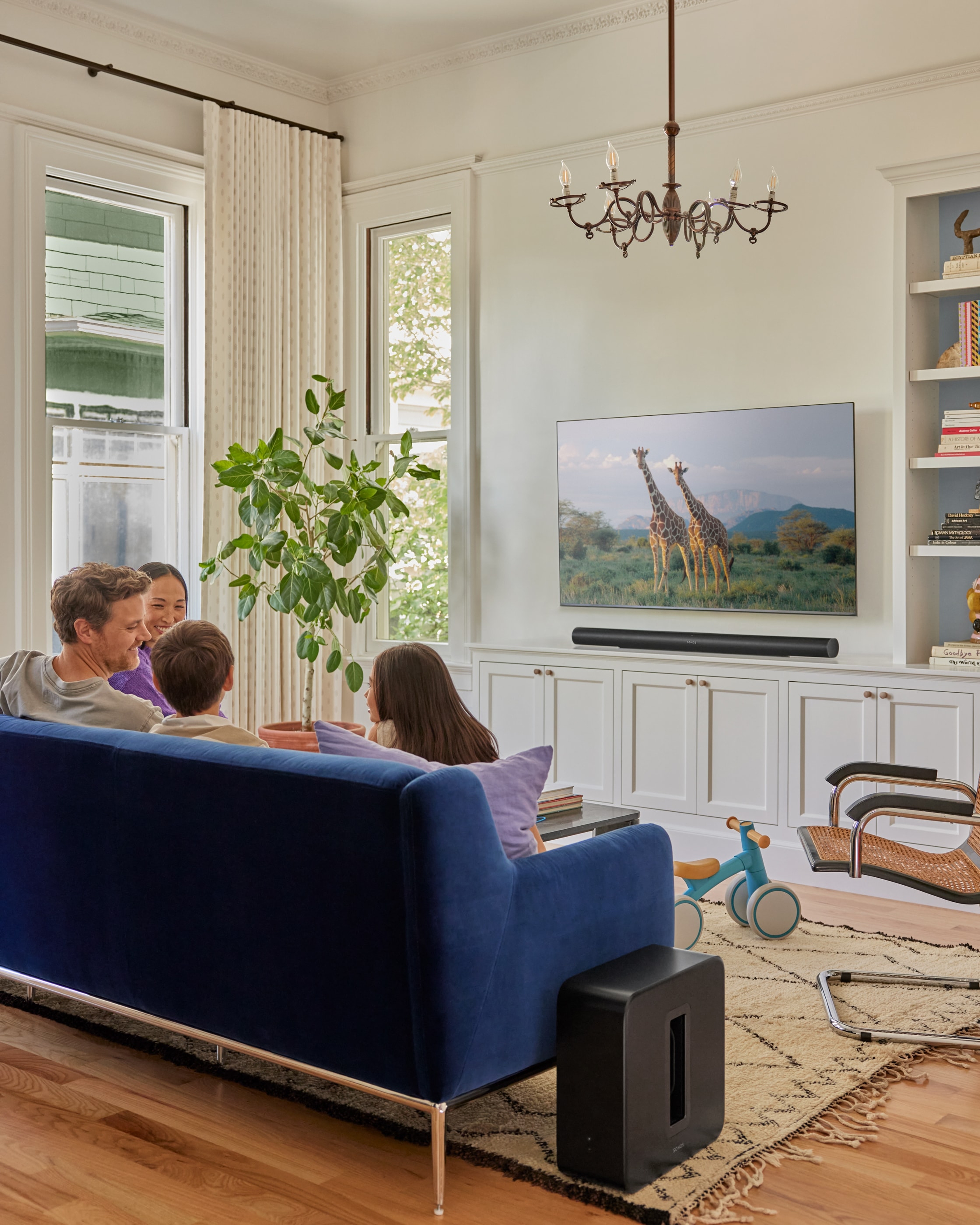 Famille assise sur un canapé bleu dans le salon avec un Sonos Sub 4 et une Sonos Arc Ultra