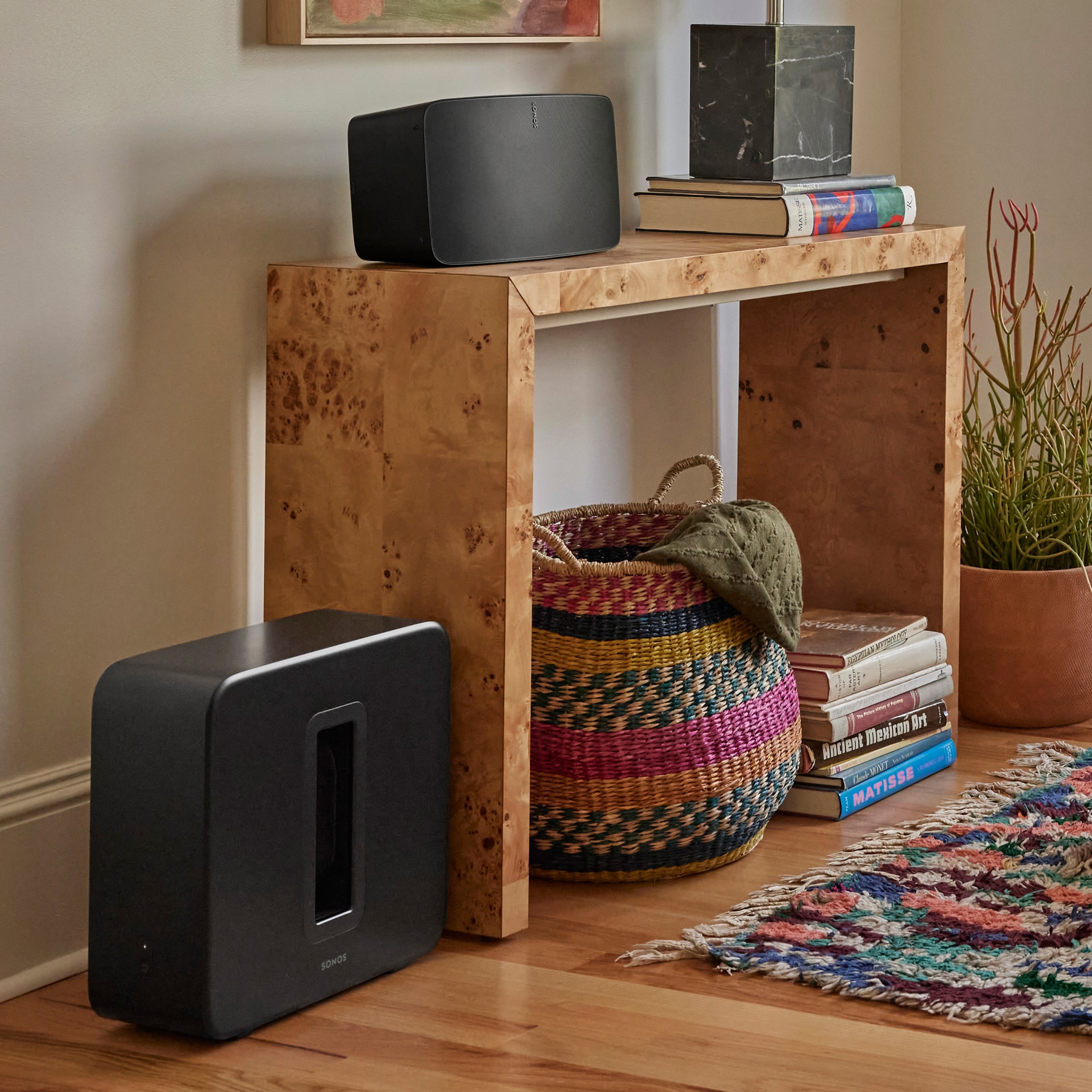 A black Sub 4 against a wall next to a table being used with a black Sonos Five