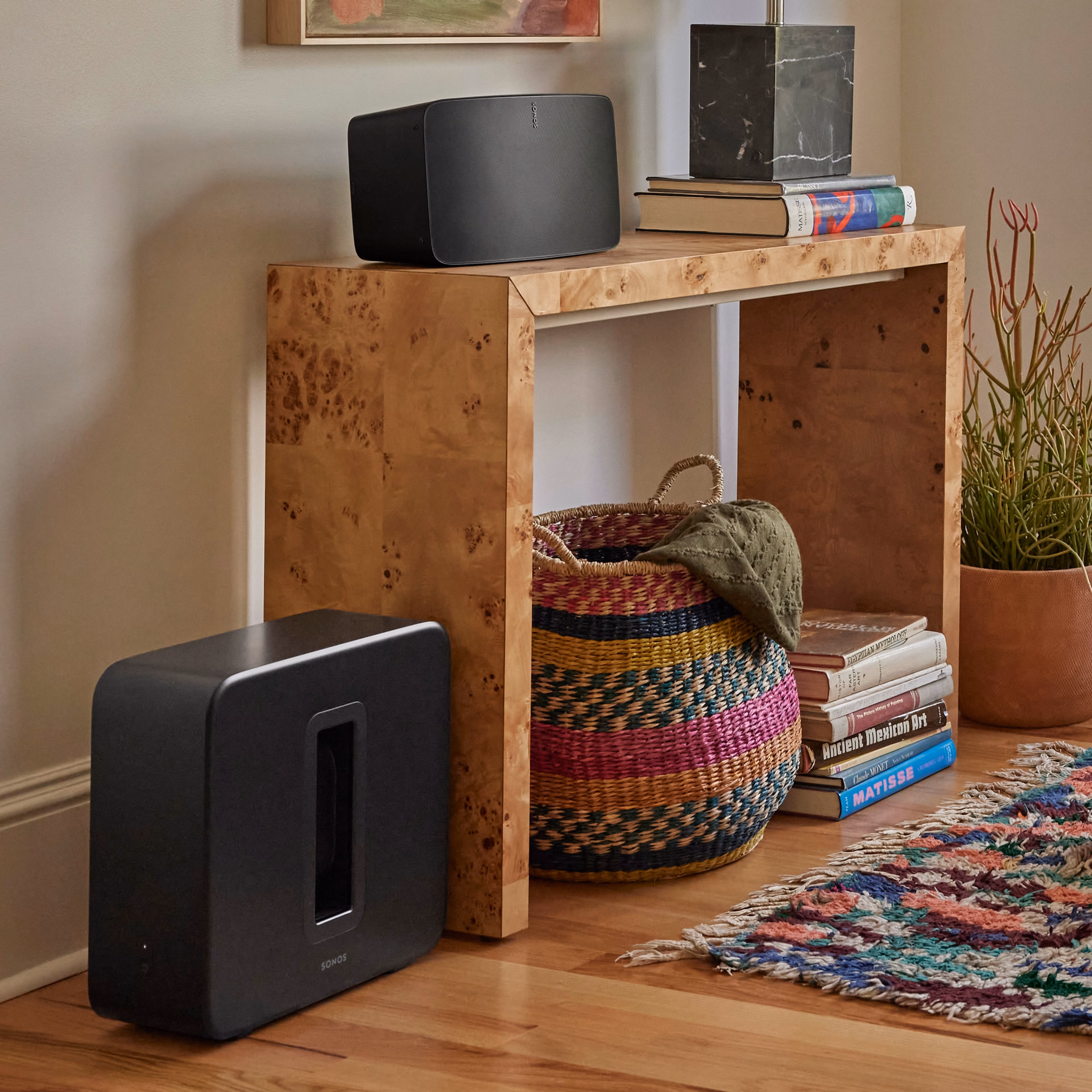 A black Sub 4 against a wall next to a table being used with a black Sonos Five