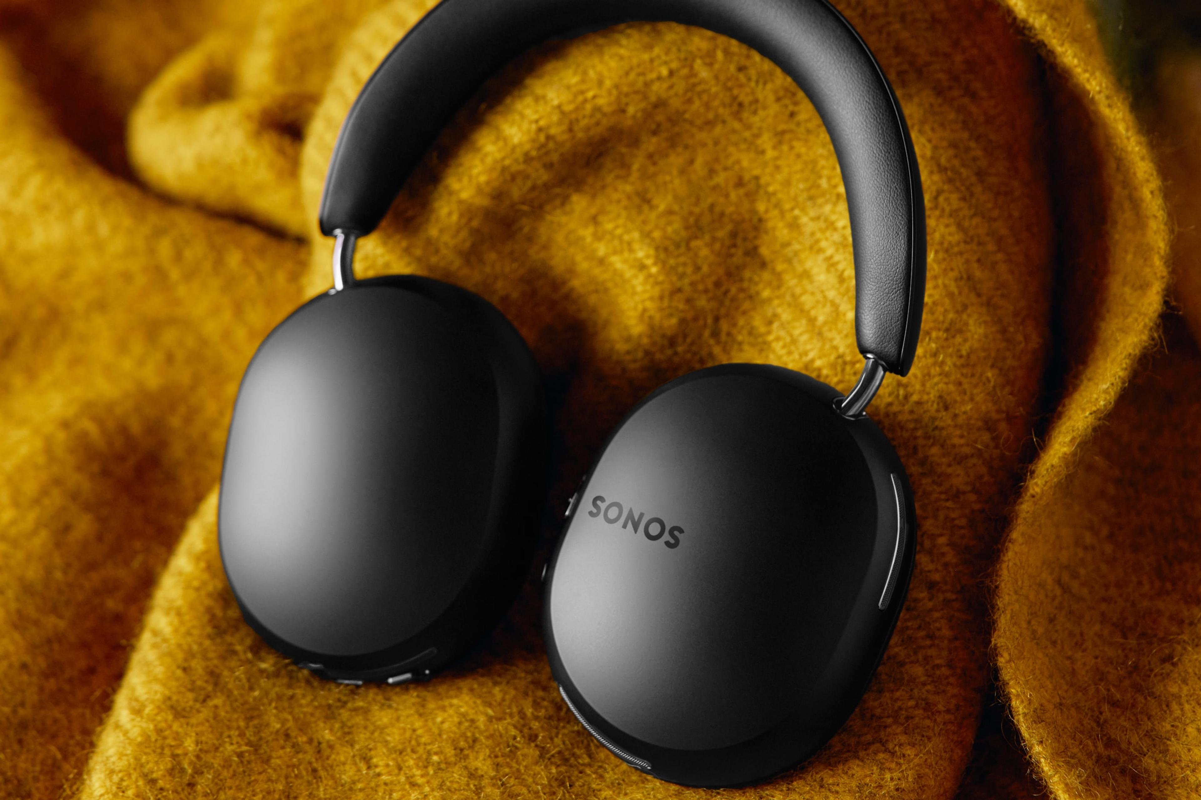 A pair of black Sonos Ace headphones on a yellow blanket