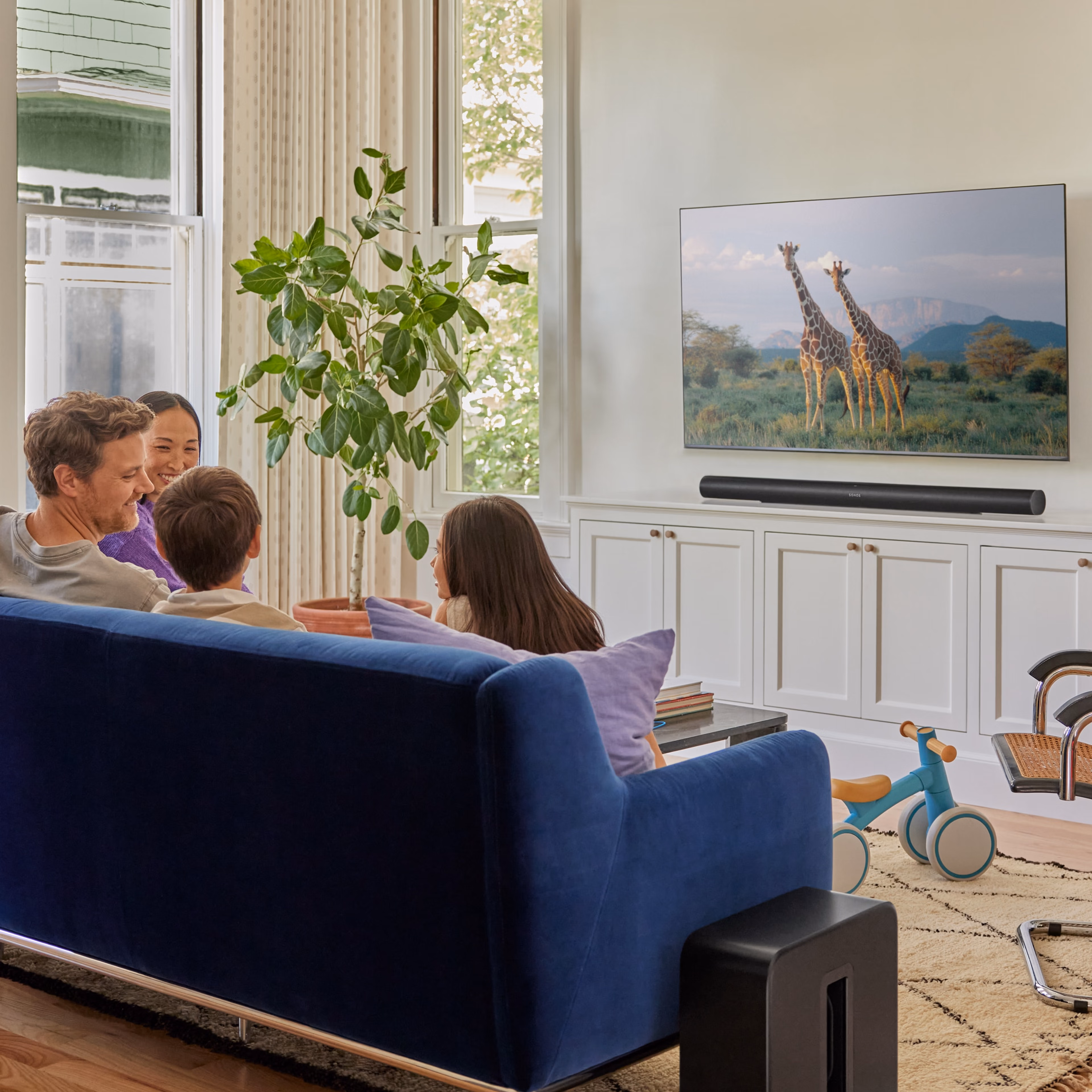 En familj som sitter i soffan och tittar på tv med en svart Arc Ultra och en svart Sub 4