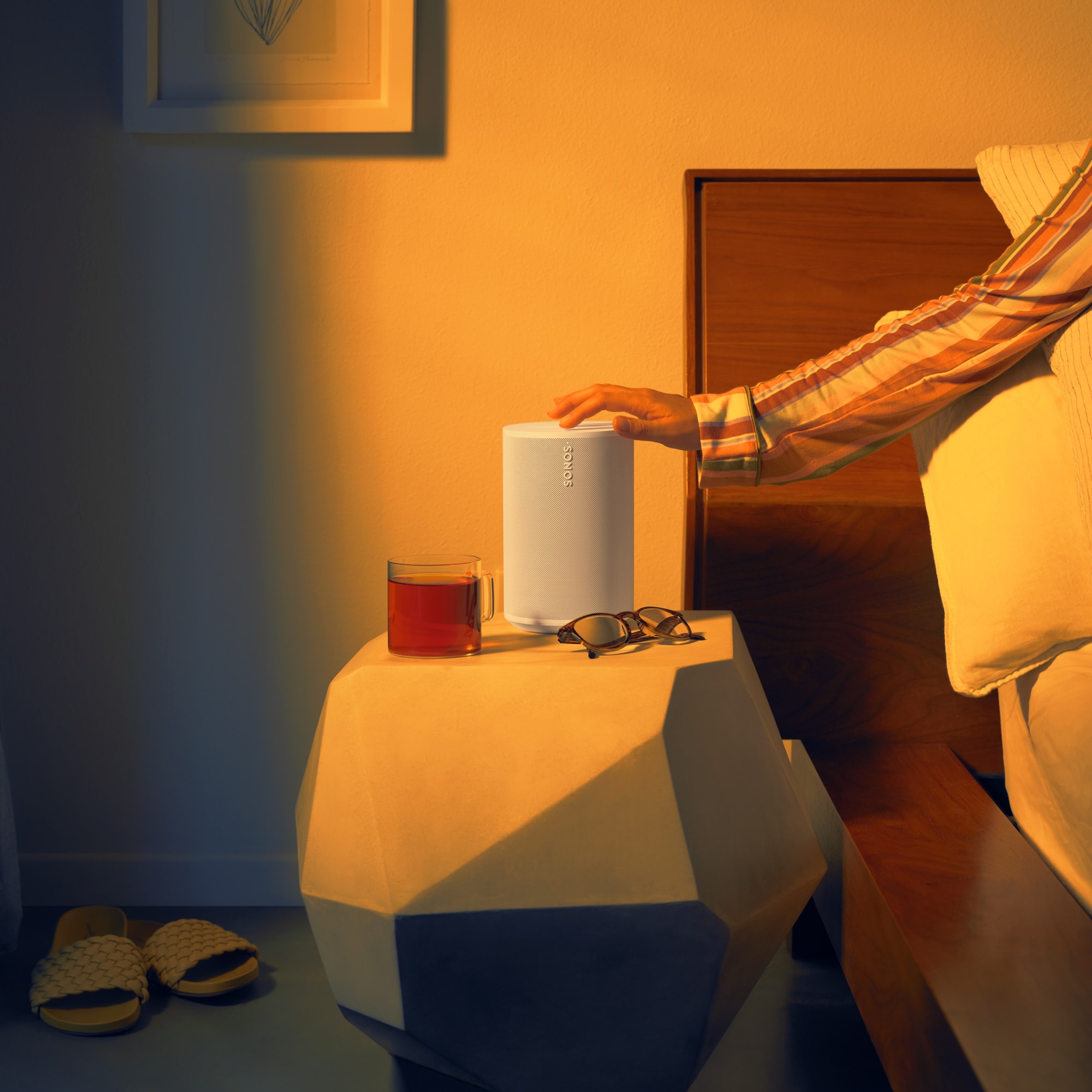 Un utilisateur se servant des commandes tactiles d'une enceinte Sonos Era 100 blanche près de son lit