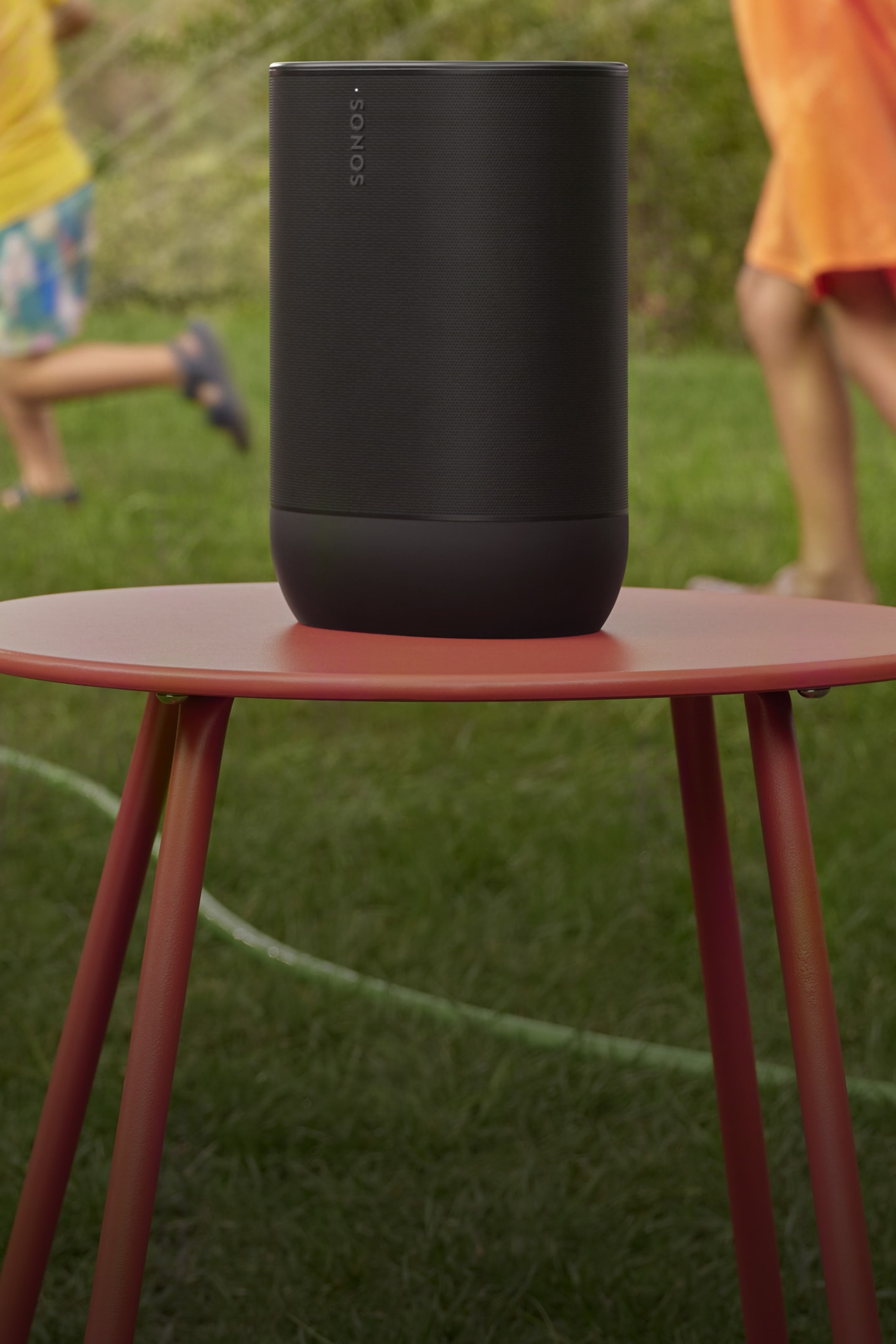 A pair of black Roam 2 portable speakers on a table with plates of food at a summer party