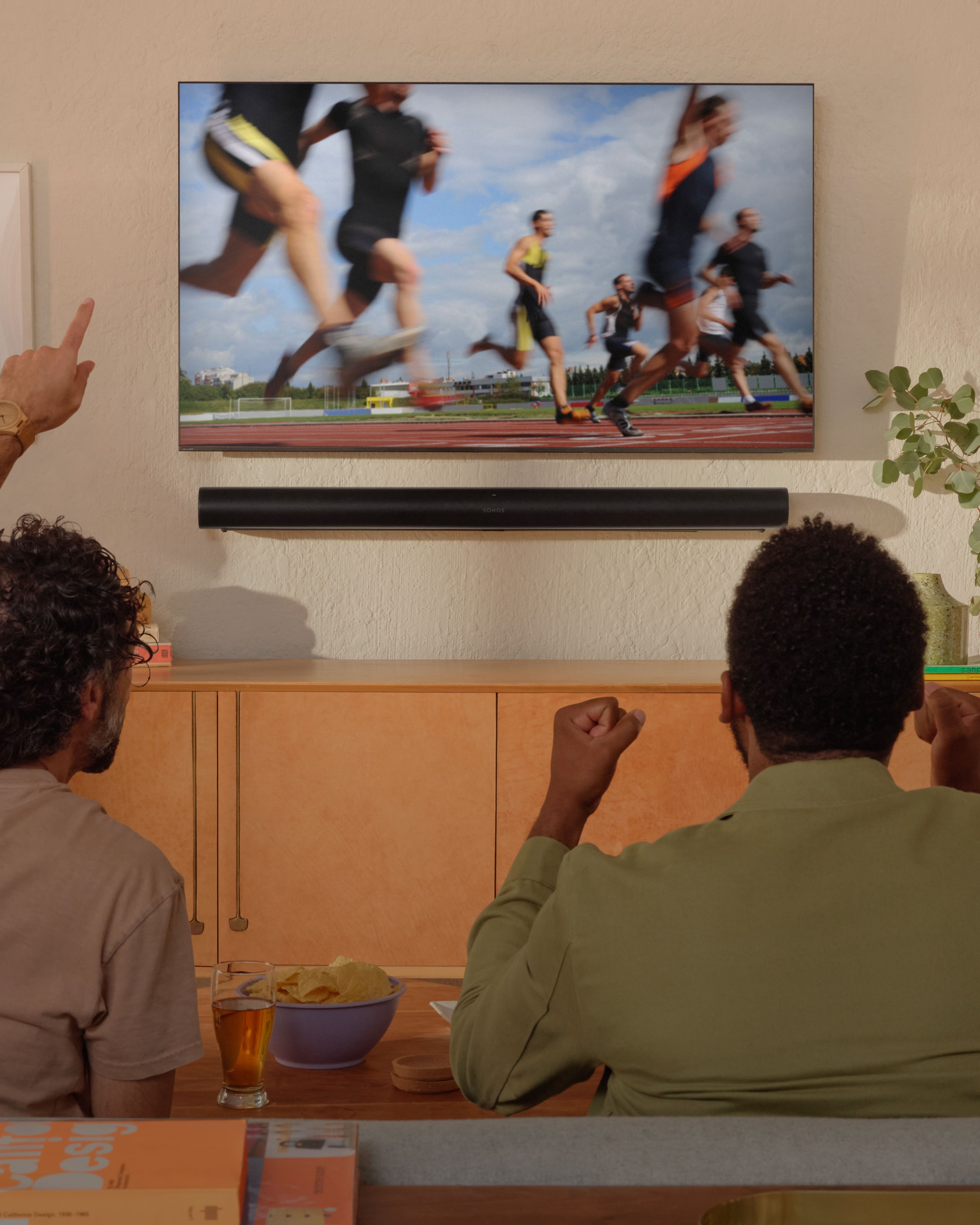 Deux personnes regardent l'athlétisme à la TV avec une Sonos Arc fixée au mur