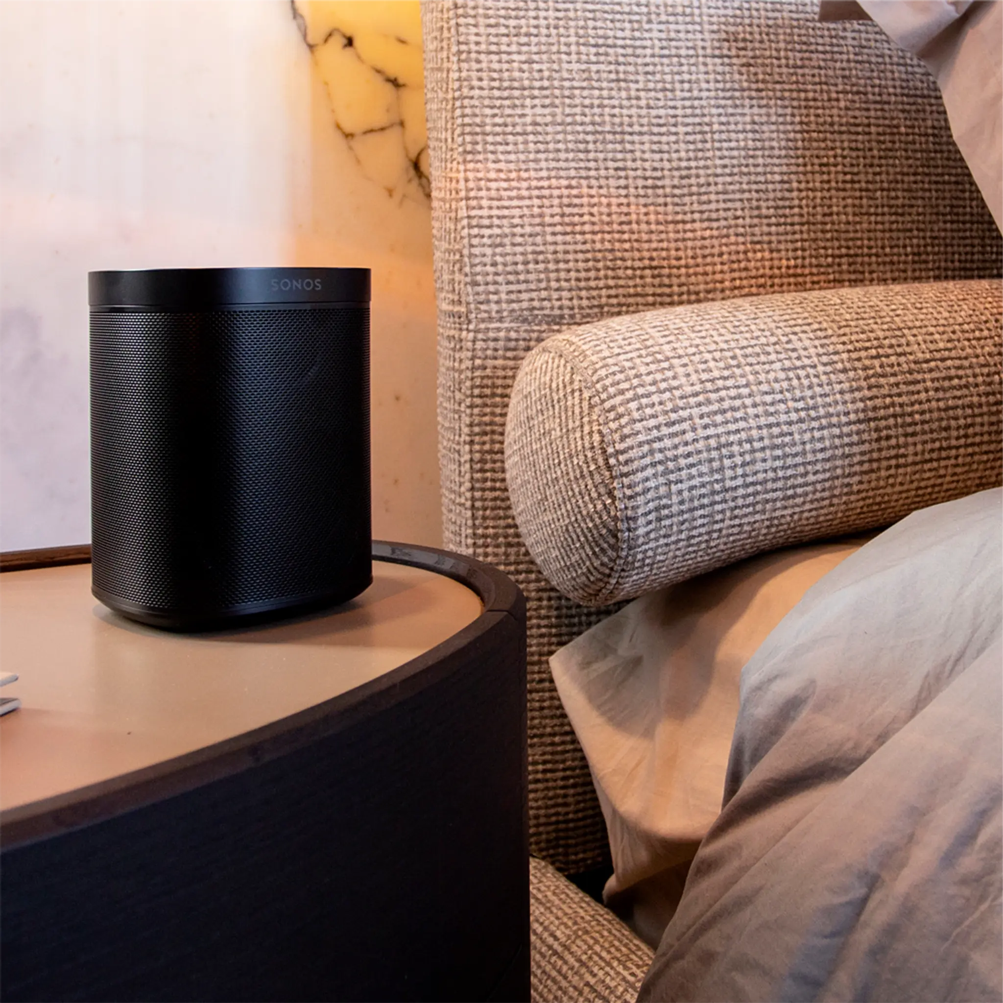 A Sonos One on a nightstand next to a bed