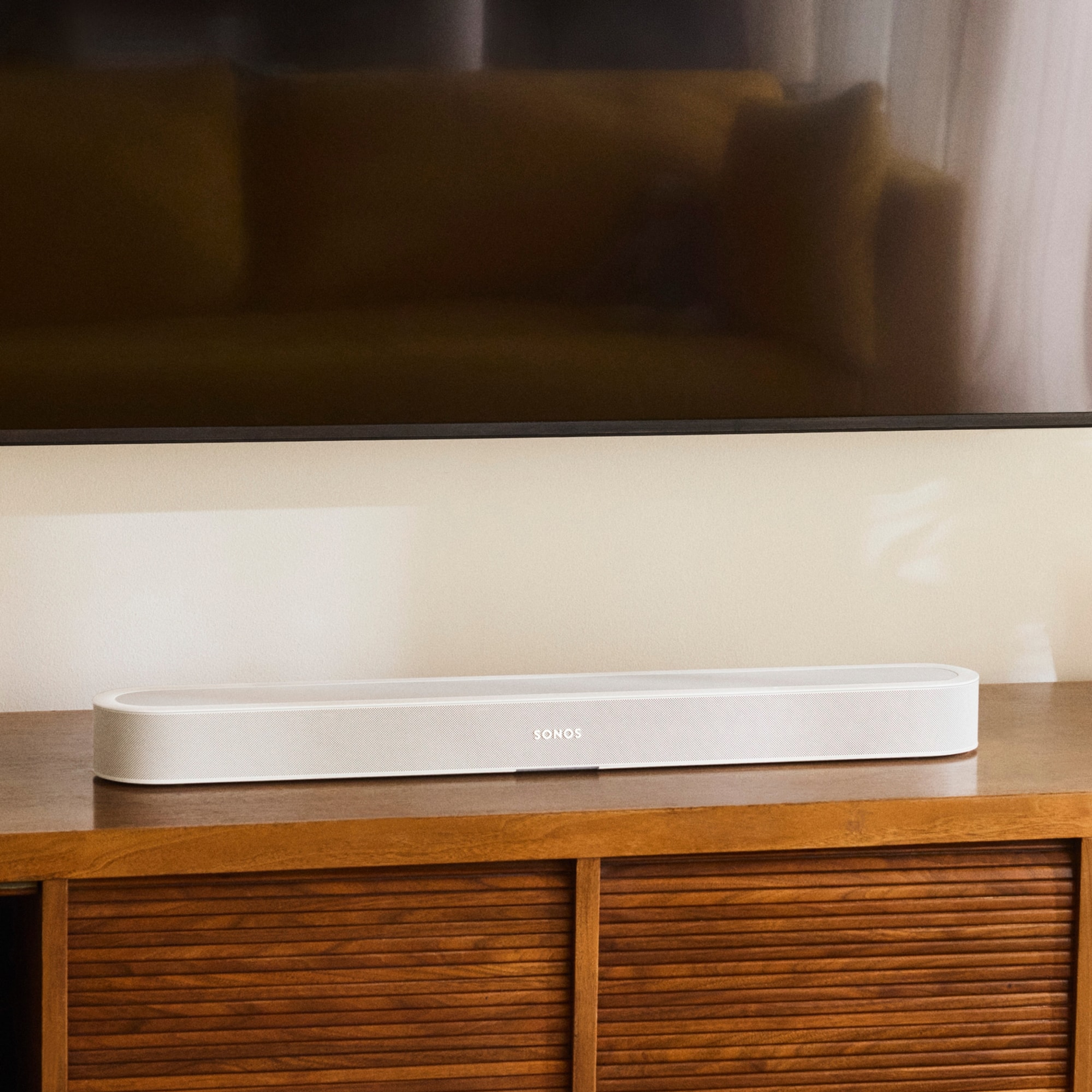 A white Sonos Beam Ultra soundbar on a wooden TV stand below a TV
