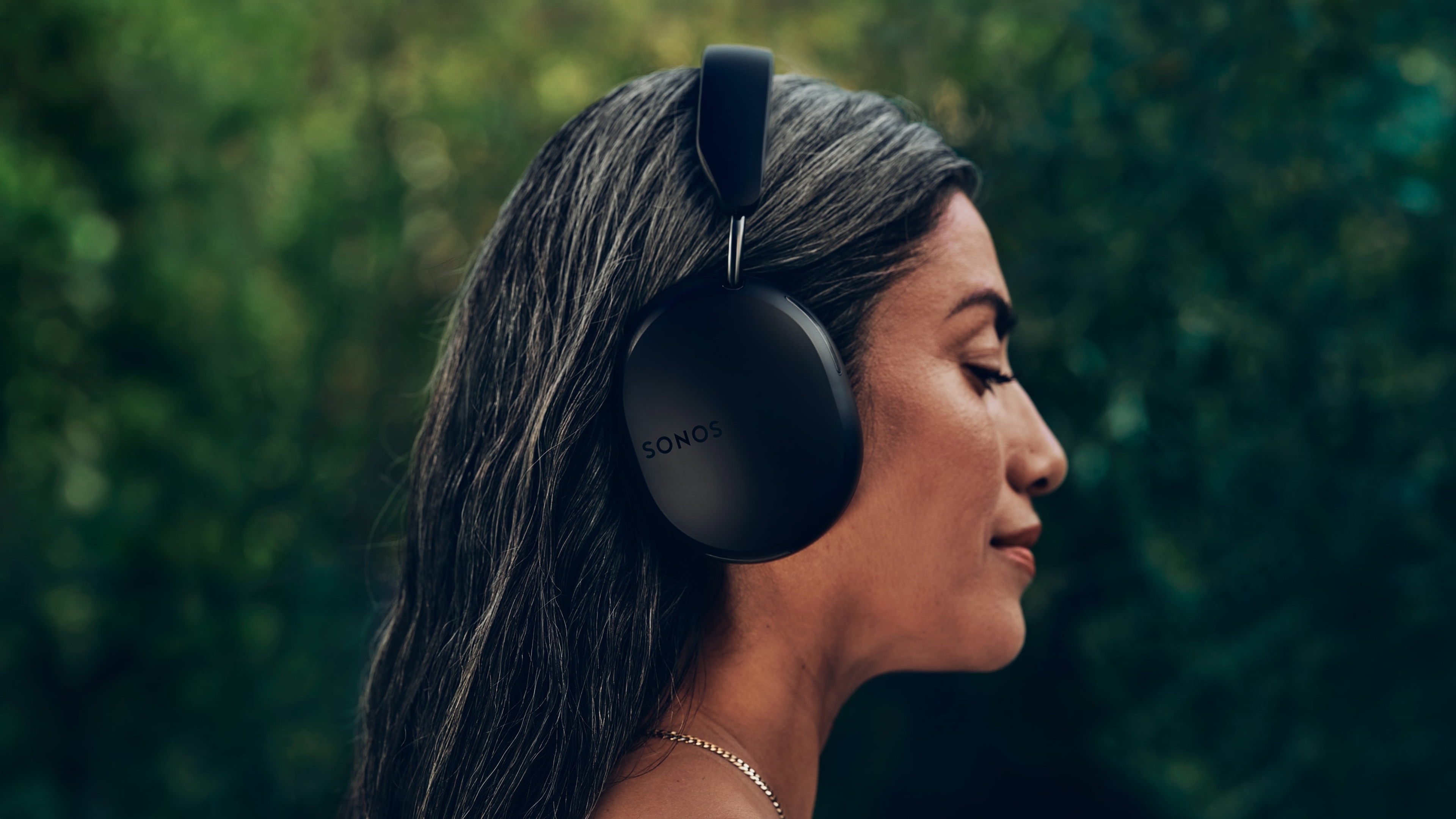 Side profile of a female user wearing a pair of black Sonos Ace headphones