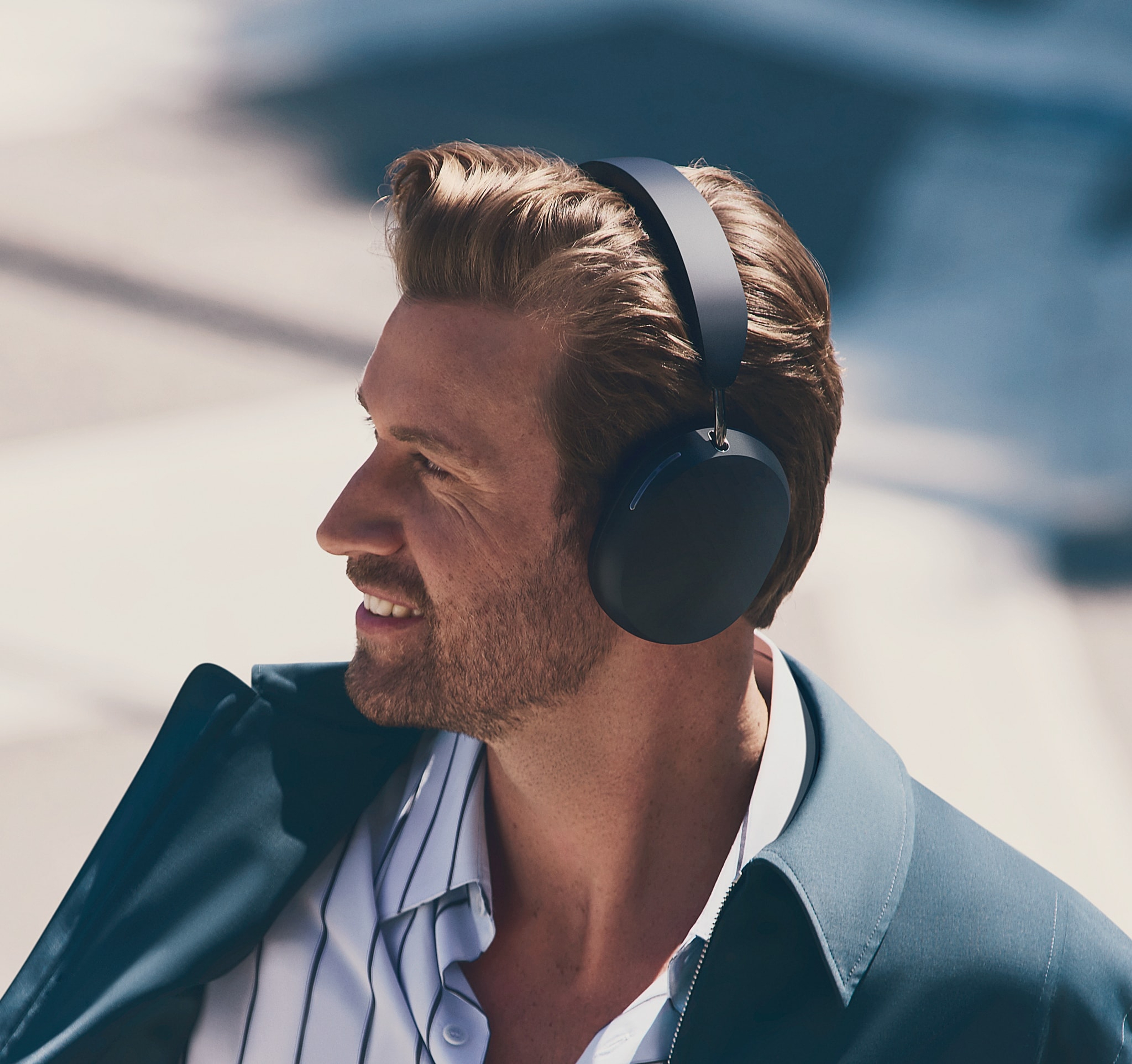 Person dressed in a suit wearing black Sonos Ace headphones outside